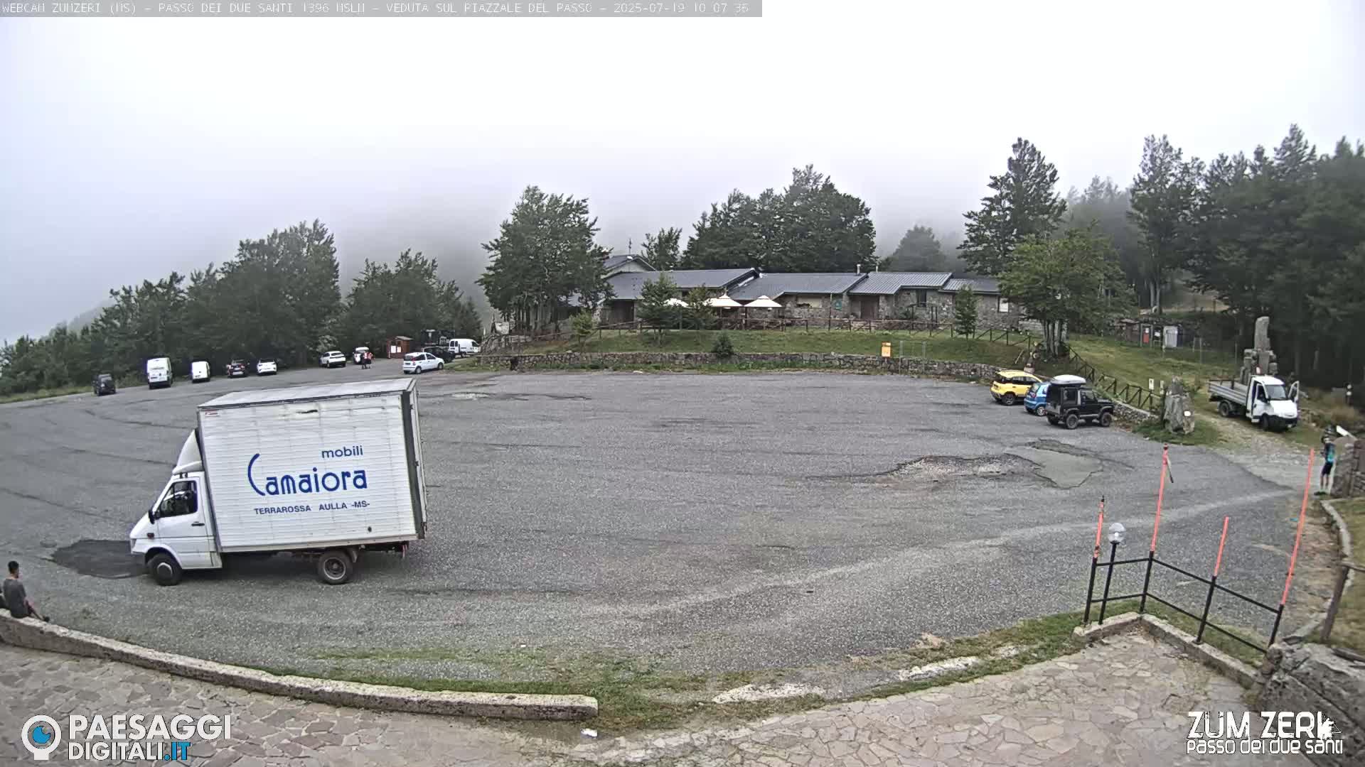 A mostly empty parking lot sits in front of a building surrounded by trees in foggy conditions.