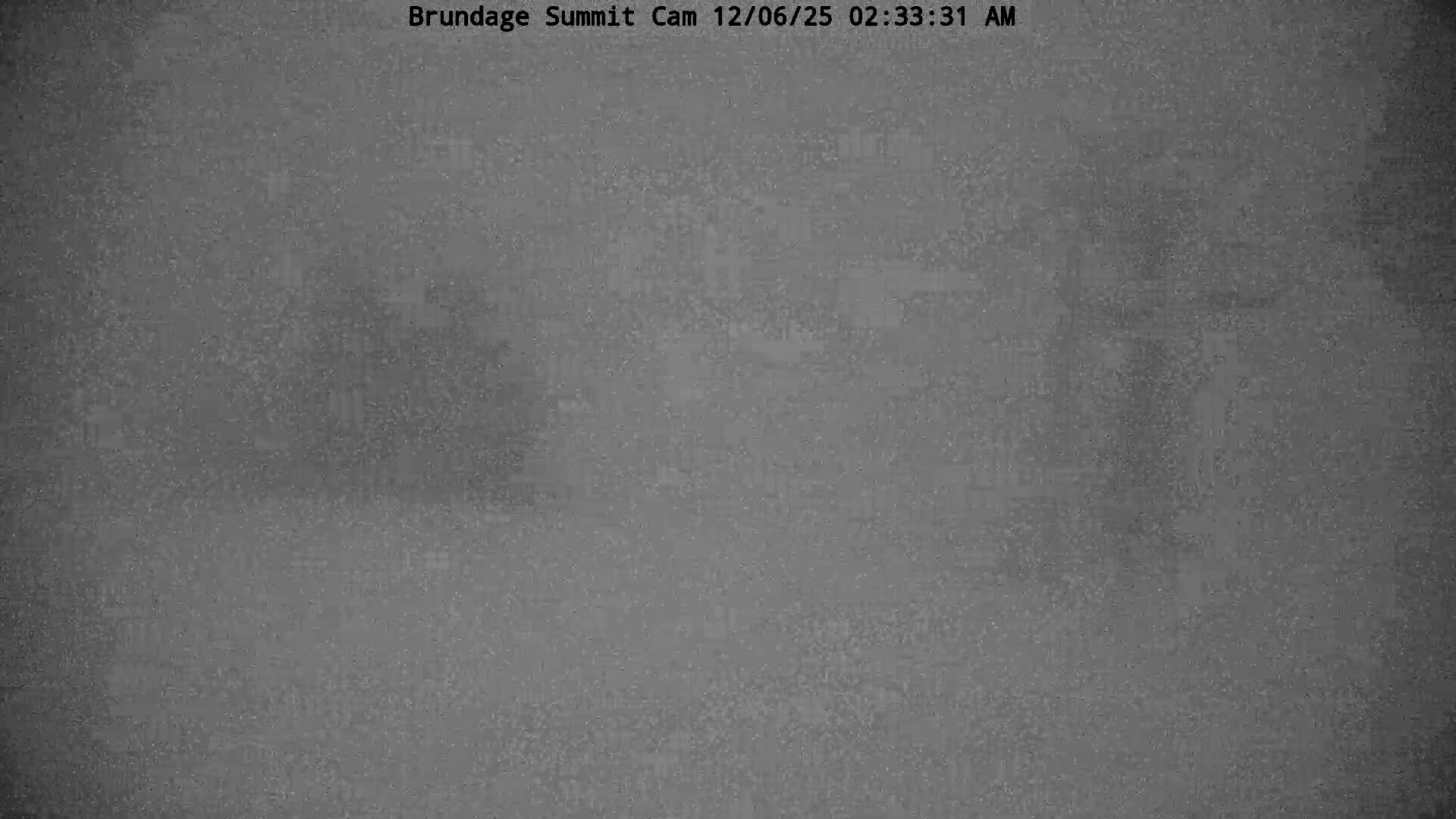 An extremely dark and grainy outdoor scene at night with very low visibility, possibly due to heavy fog or snowfall, makes the landscape appear as faint, indistinct grey variations.