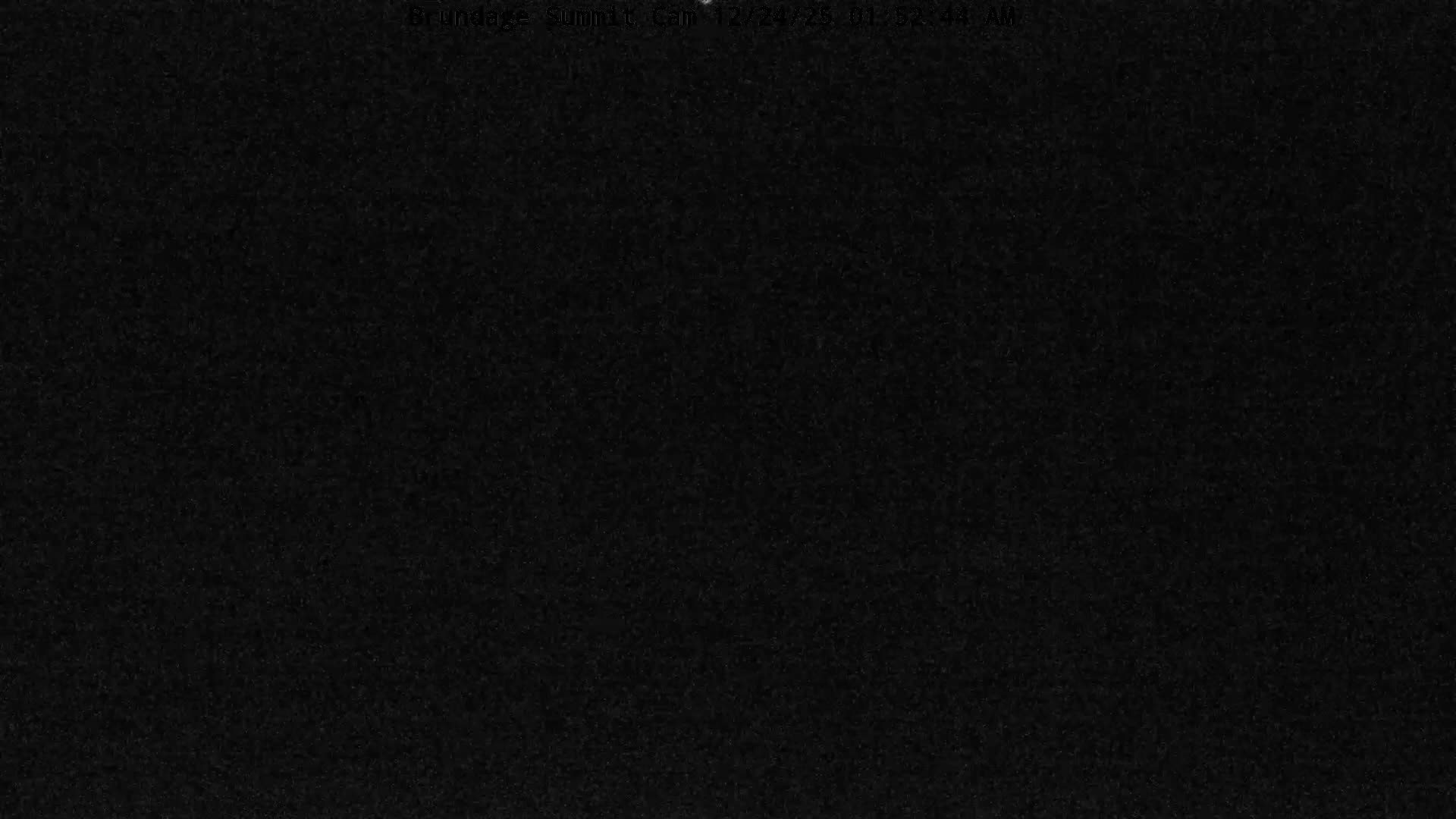 An extremely dark and grainy outdoor scene at night with very low visibility, possibly due to heavy fog or snowfall, makes the landscape appear as faint, indistinct grey variations.