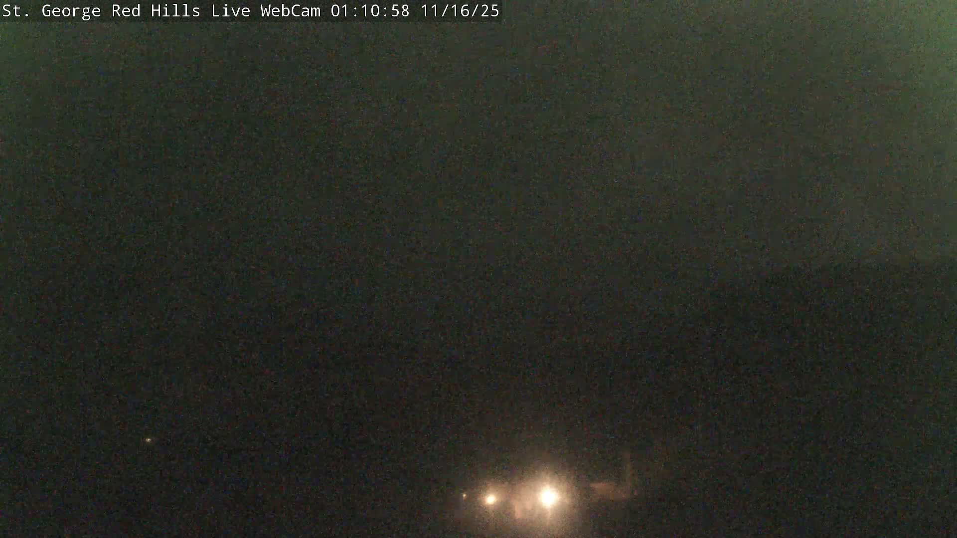 A dark, grainy outdoor scene at night features several bright lights visible through low visibility conditions, suggesting fog or heavy mist.