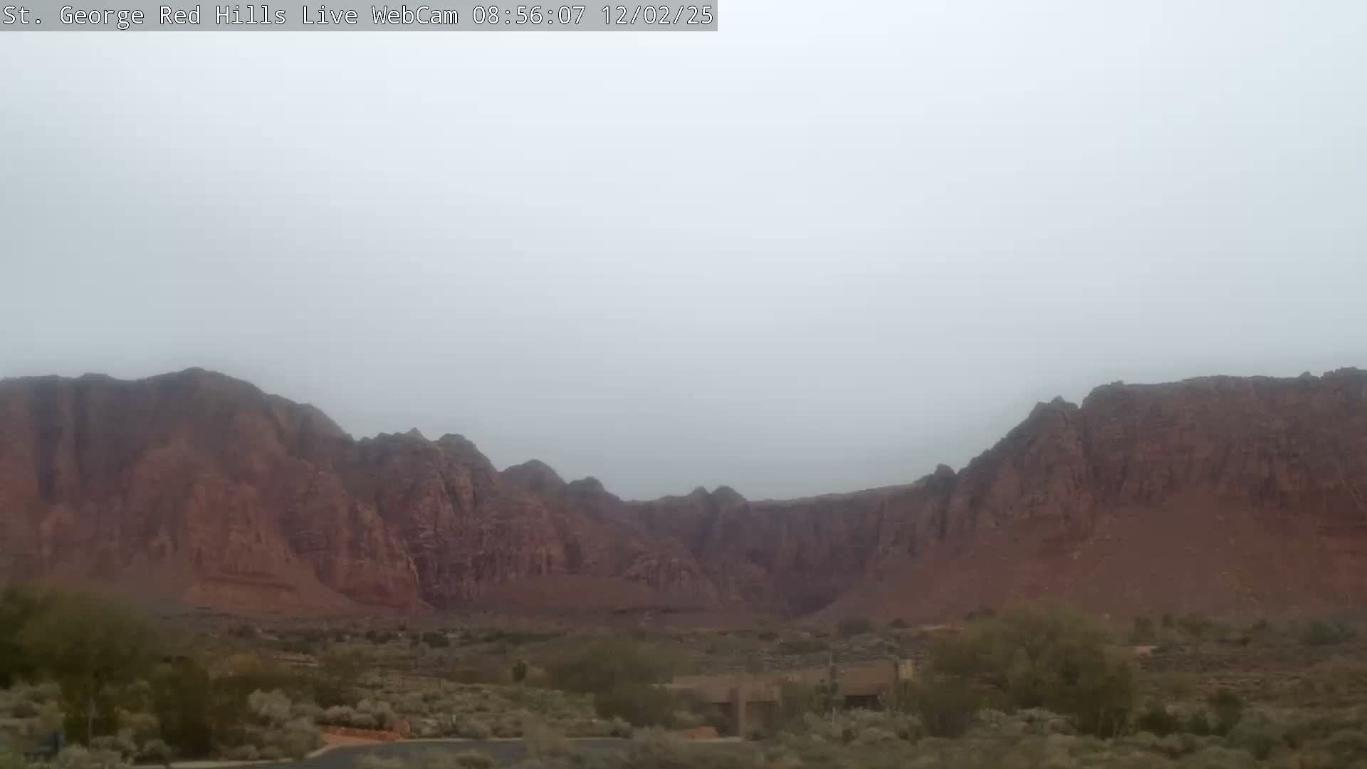 A wide landscape view features reddish-brown mountains and desert vegetation under a heavily overcast or foggy sky.