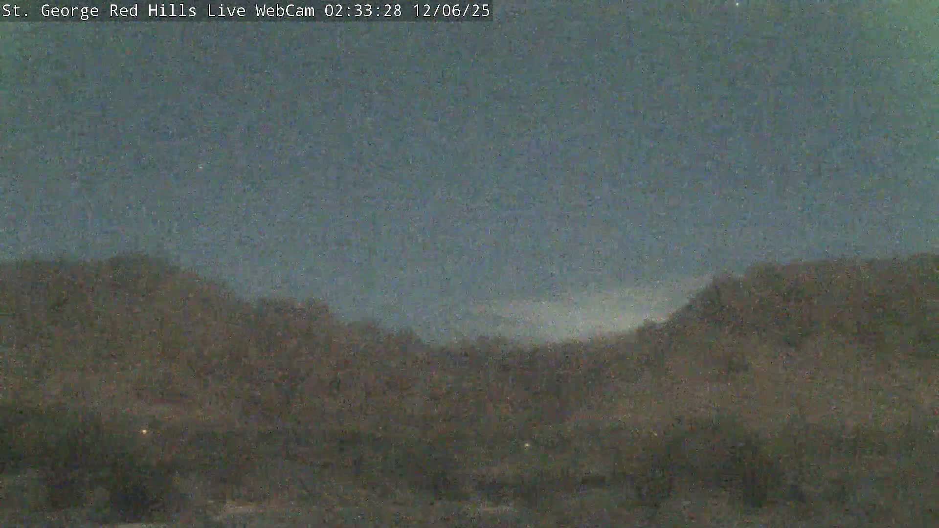 A dark and grainy nighttime landscape features rolling hills beneath a hazy or partly cloudy sky.