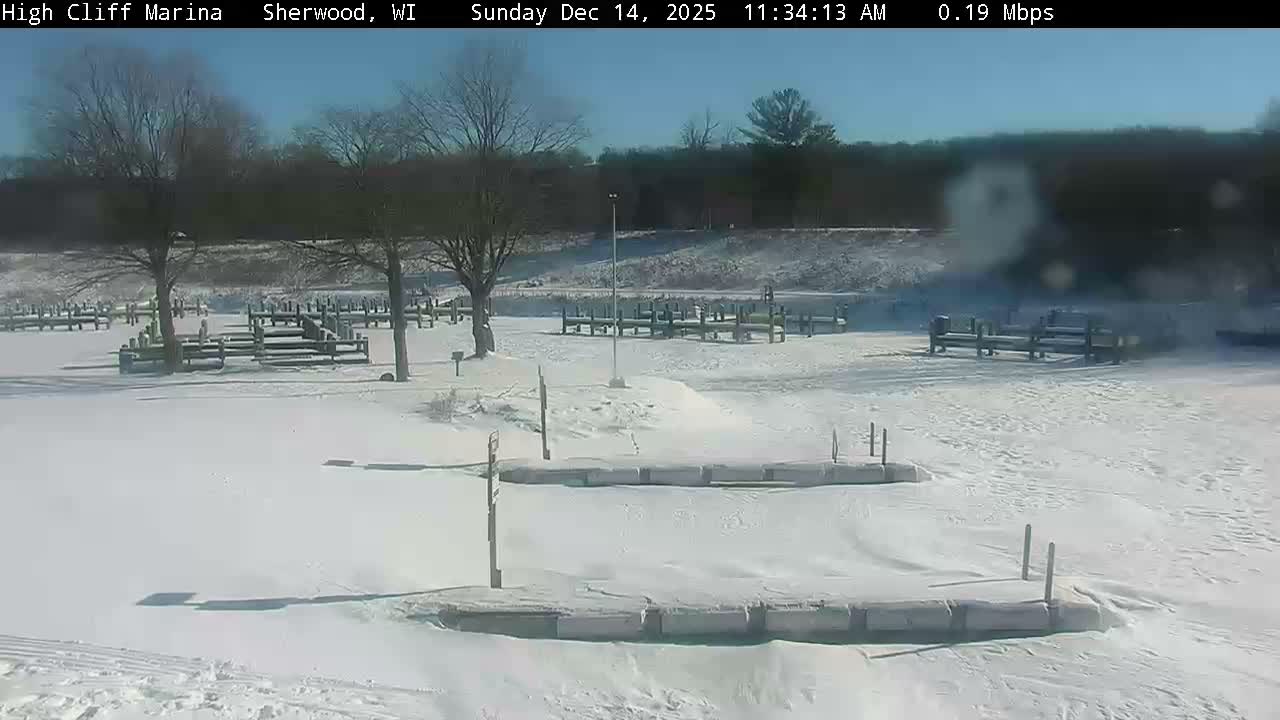 A snow-covered marina at night is brightly illuminated by a single light source, revealing docks extending into what appears to be partially frozen water under clear, cold conditions.