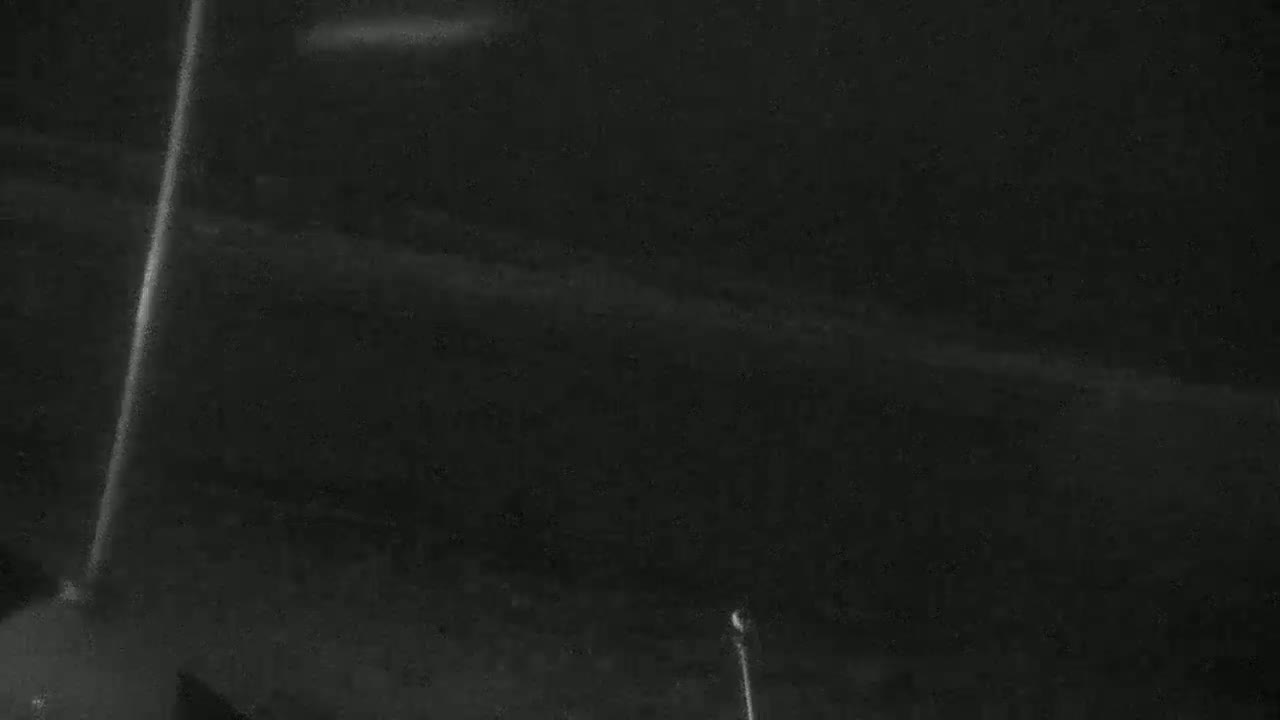 A low-light, possibly nighttime, outdoor scene shows a dark, indistinct landscape with a bright vertical line suggesting a light source or glare.