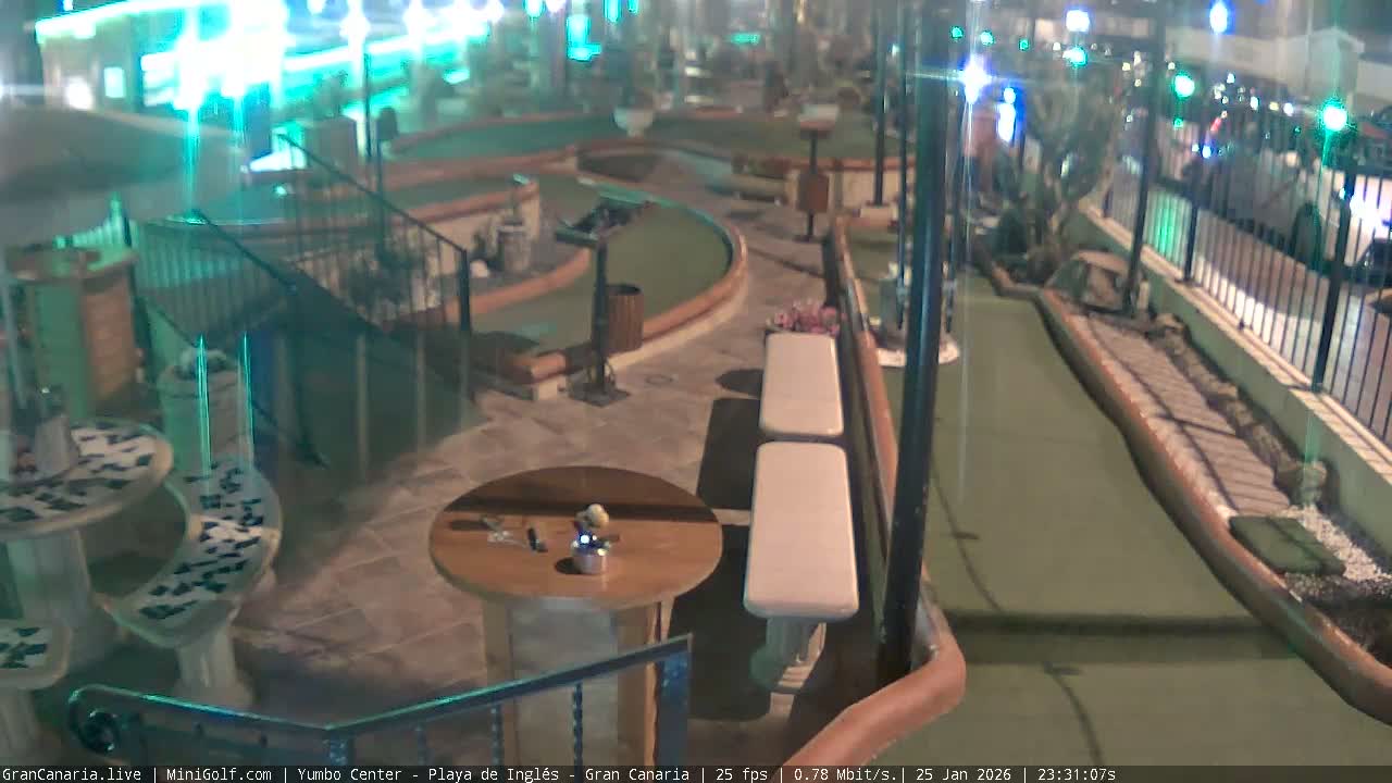 An outdoor mini-golf course is visible at night, brightly illuminated by a mix of colorful artificial lights under clear weather conditions.