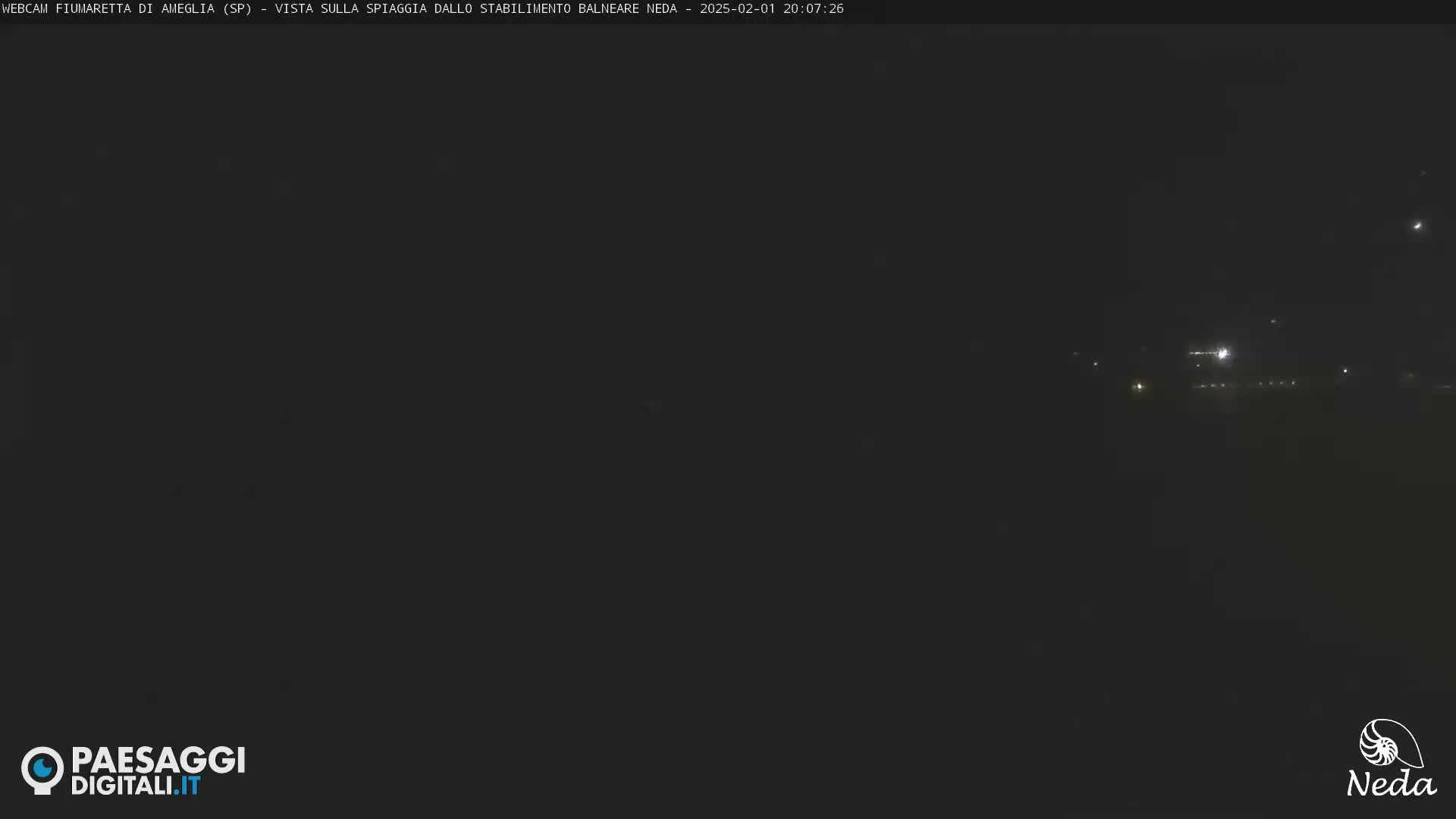 A dark, nighttime scene shows distant lights faintly illuminating a dark beach.