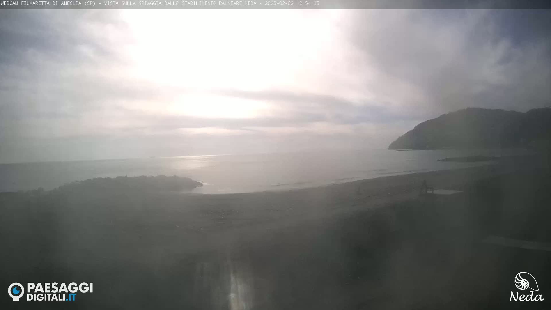 A hazy, overcast day reveals a view of a beach and calm ocean, with a distant hill shrouded in mist.