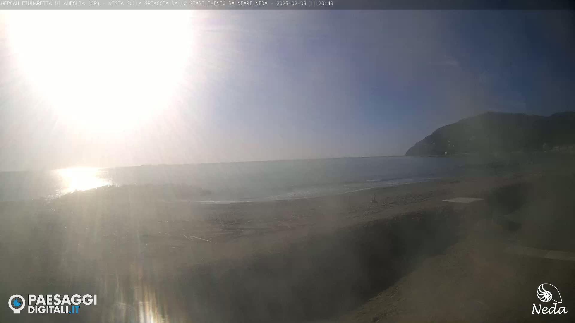 A hazy, sunny day at a sandy beach with calm ocean waters and a distant mountain in the background.