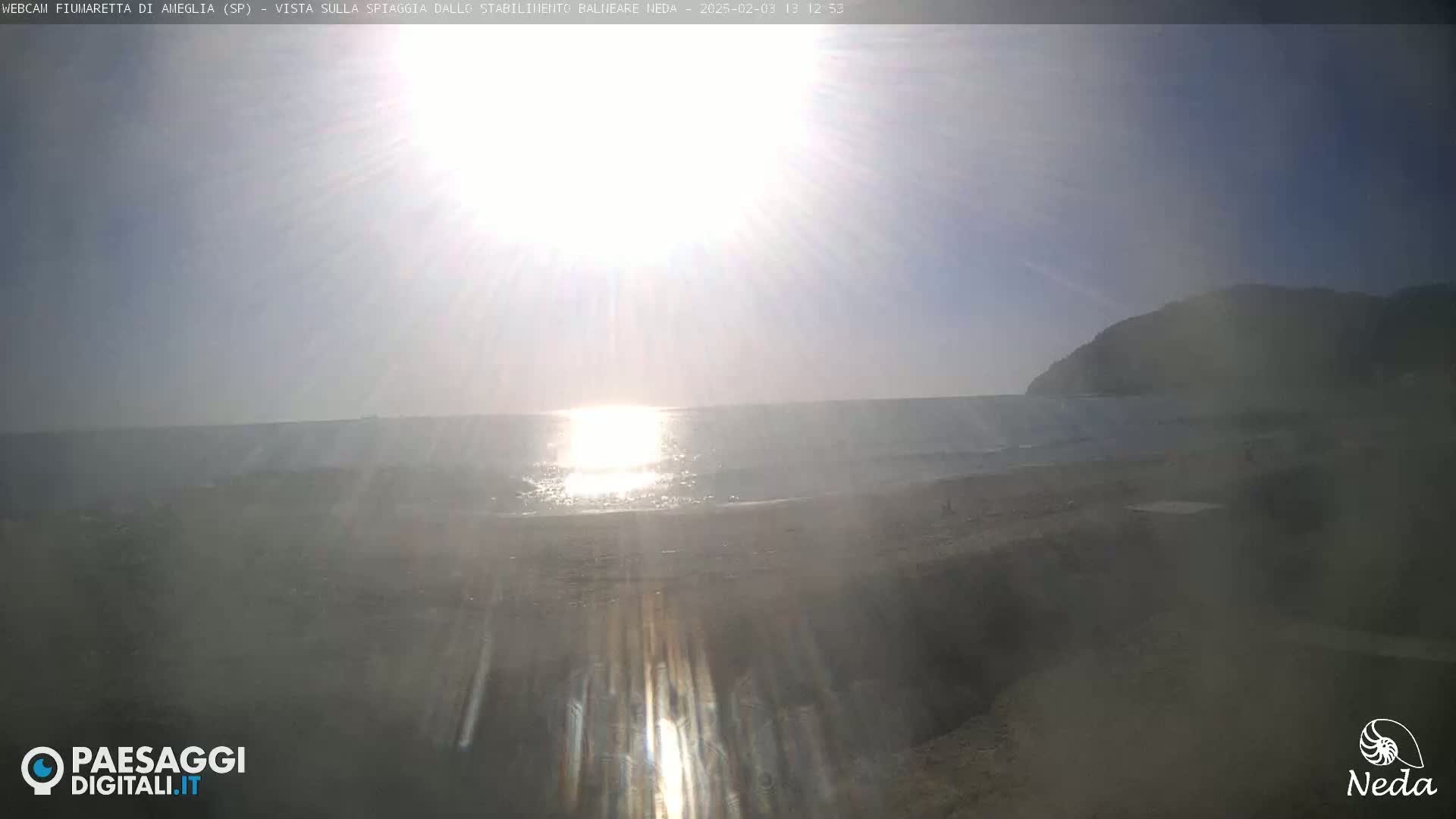 A bright, sunny day at a beach shows the ocean meeting the shore under a mostly clear sky.