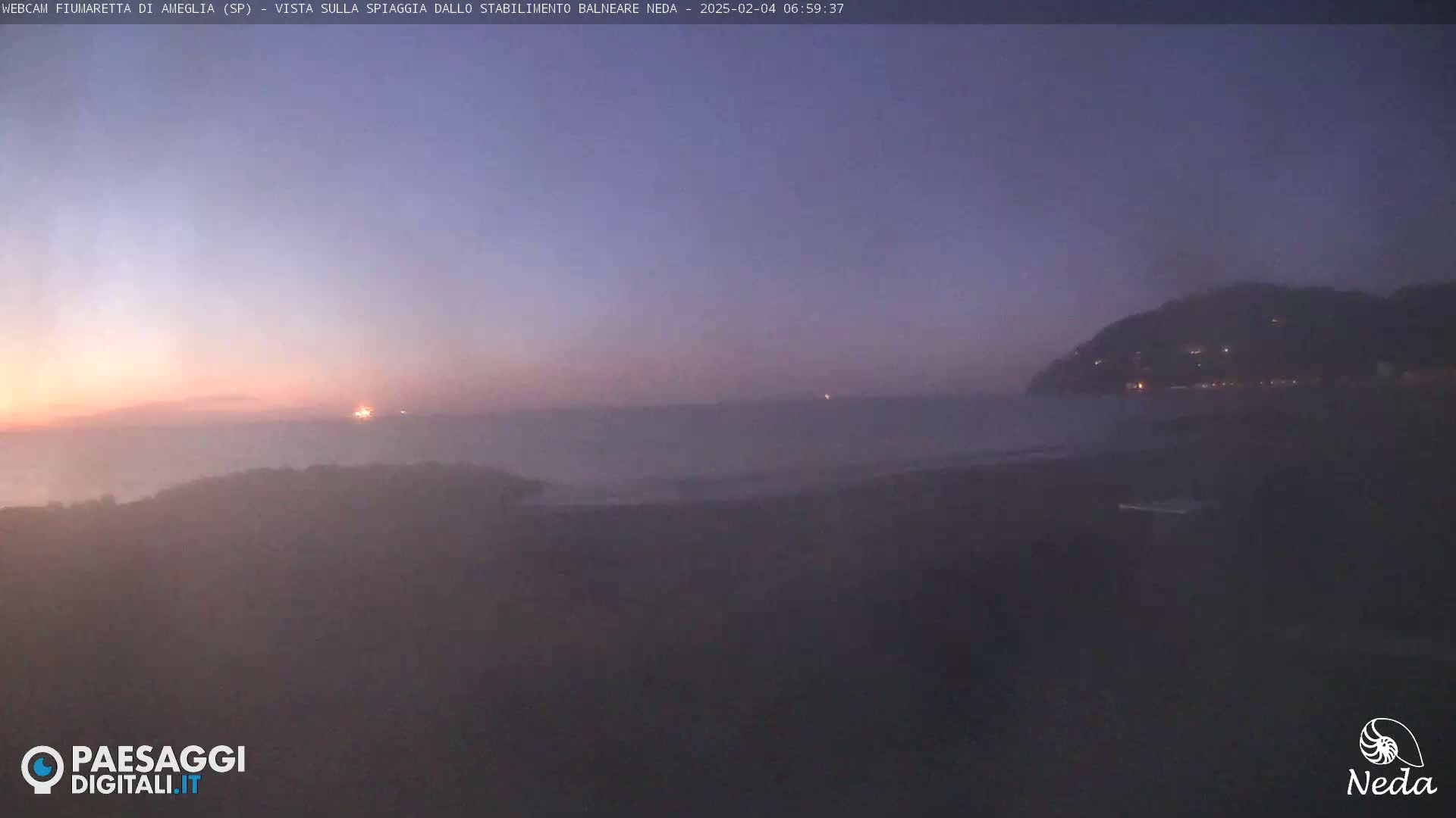 A hazy sunrise over a calm sea with a hill in the distance.