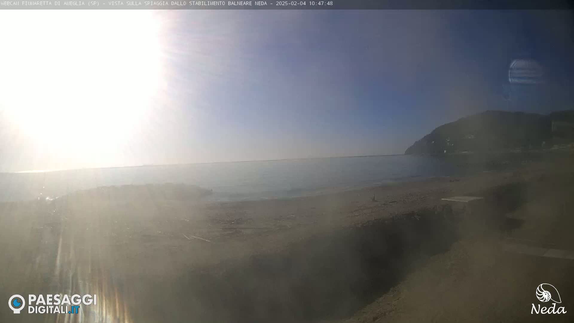 A hazy sunny day at a beach with calm water and a distant hill visible.