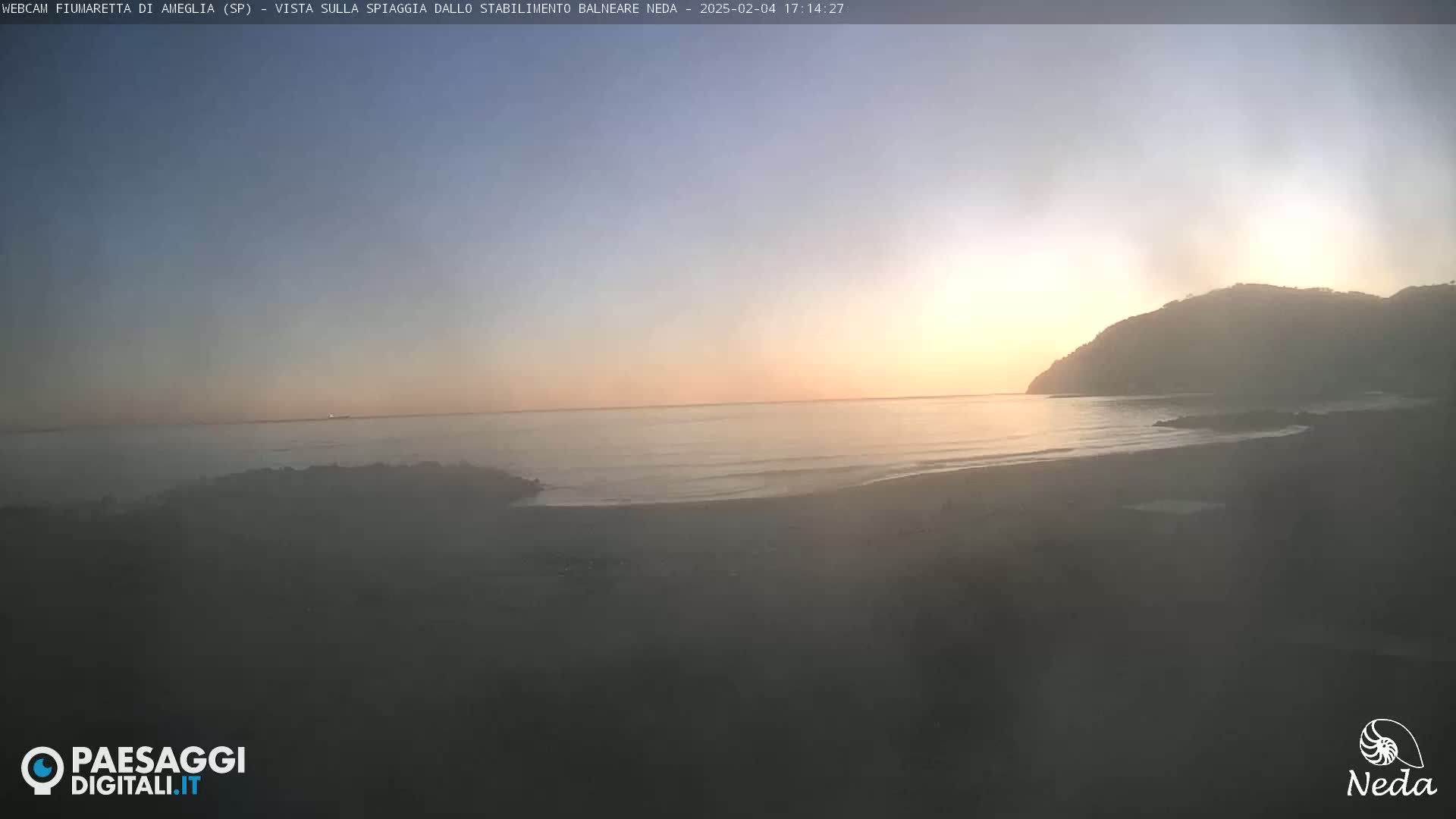 A hazy sunset over a calm ocean, with a dark hill visible in the distance.
