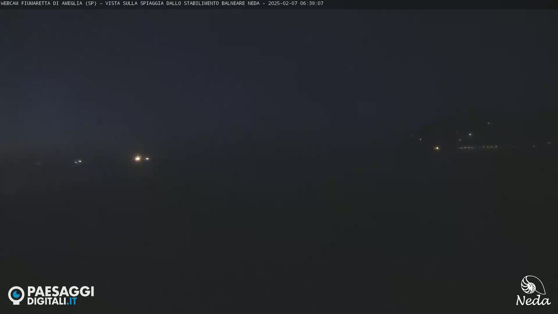 A dark, nighttime view of a distant, dimly lit shoreline.