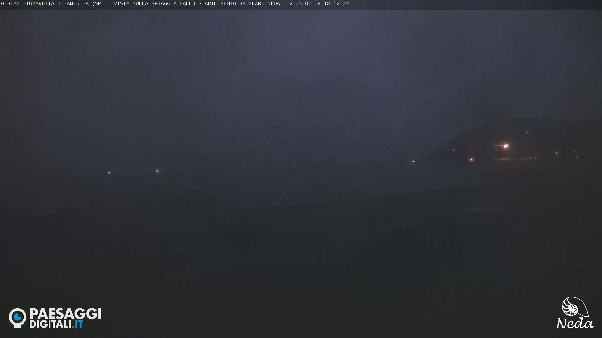 A dark, hazy night scene shows a dimly lit shoreline with a few faint lights visible in the distance.