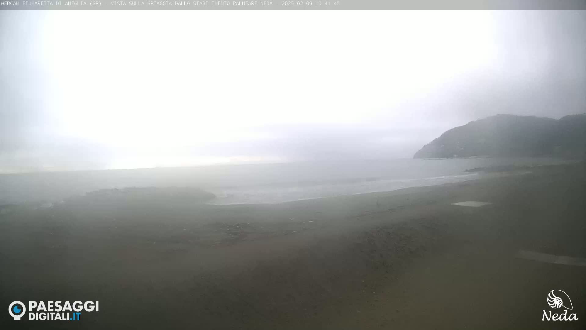 A hazy, overcast day shows a beach with a dark, distant hill under a muted sky.