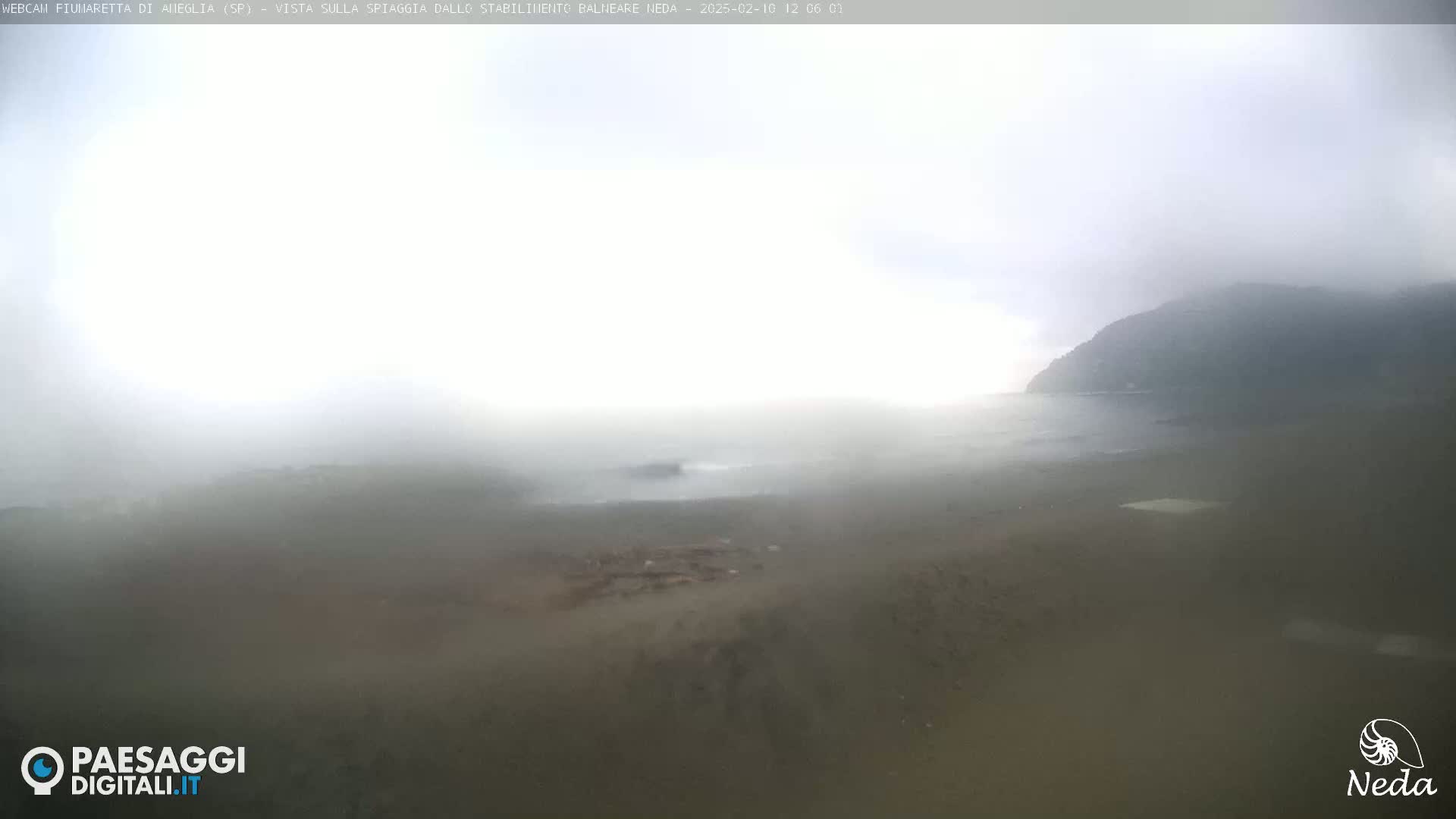 A foggy coastal scene shows a hazy beach and a distant hill shrouded in mist.
