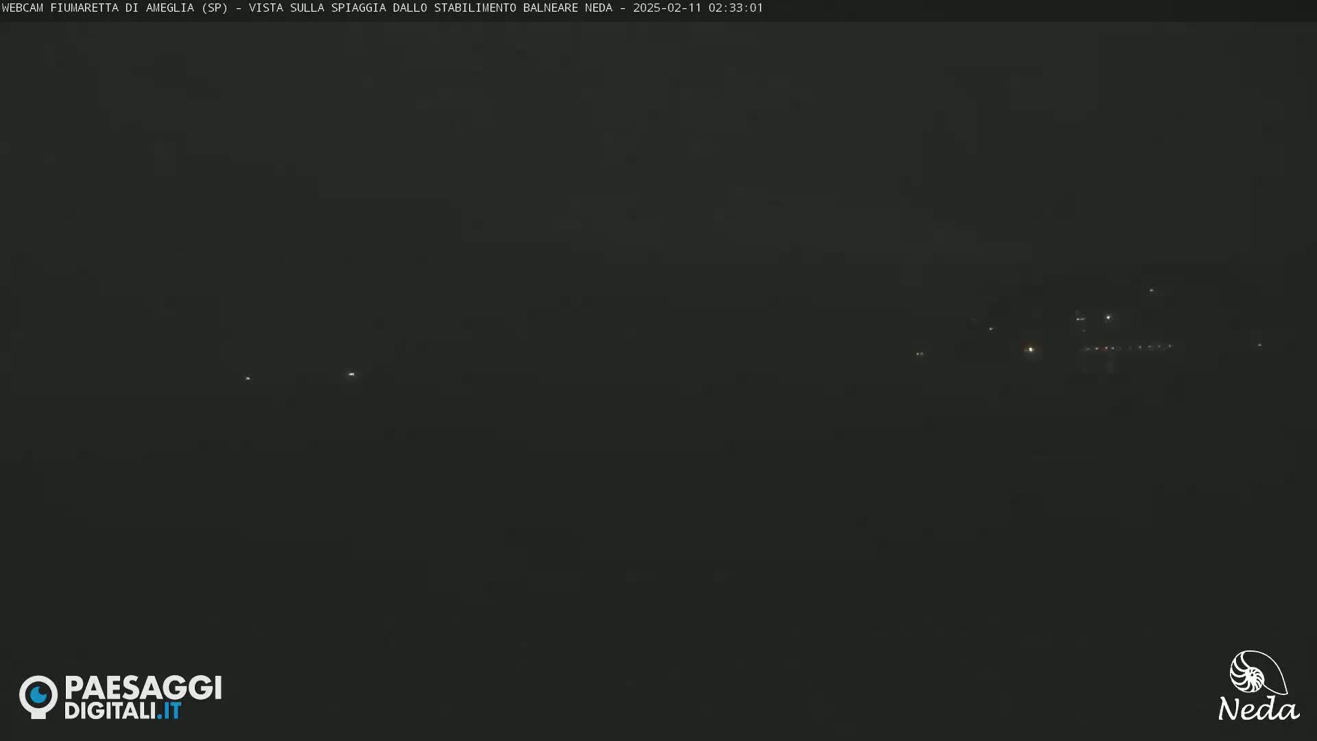 A dark, nighttime view of a distant, dimly lit shoreline.