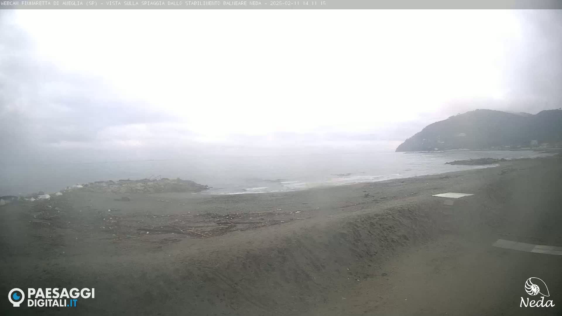 A hazy, overcast day at a beach, showing a mostly empty shoreline with a hill in the distance.