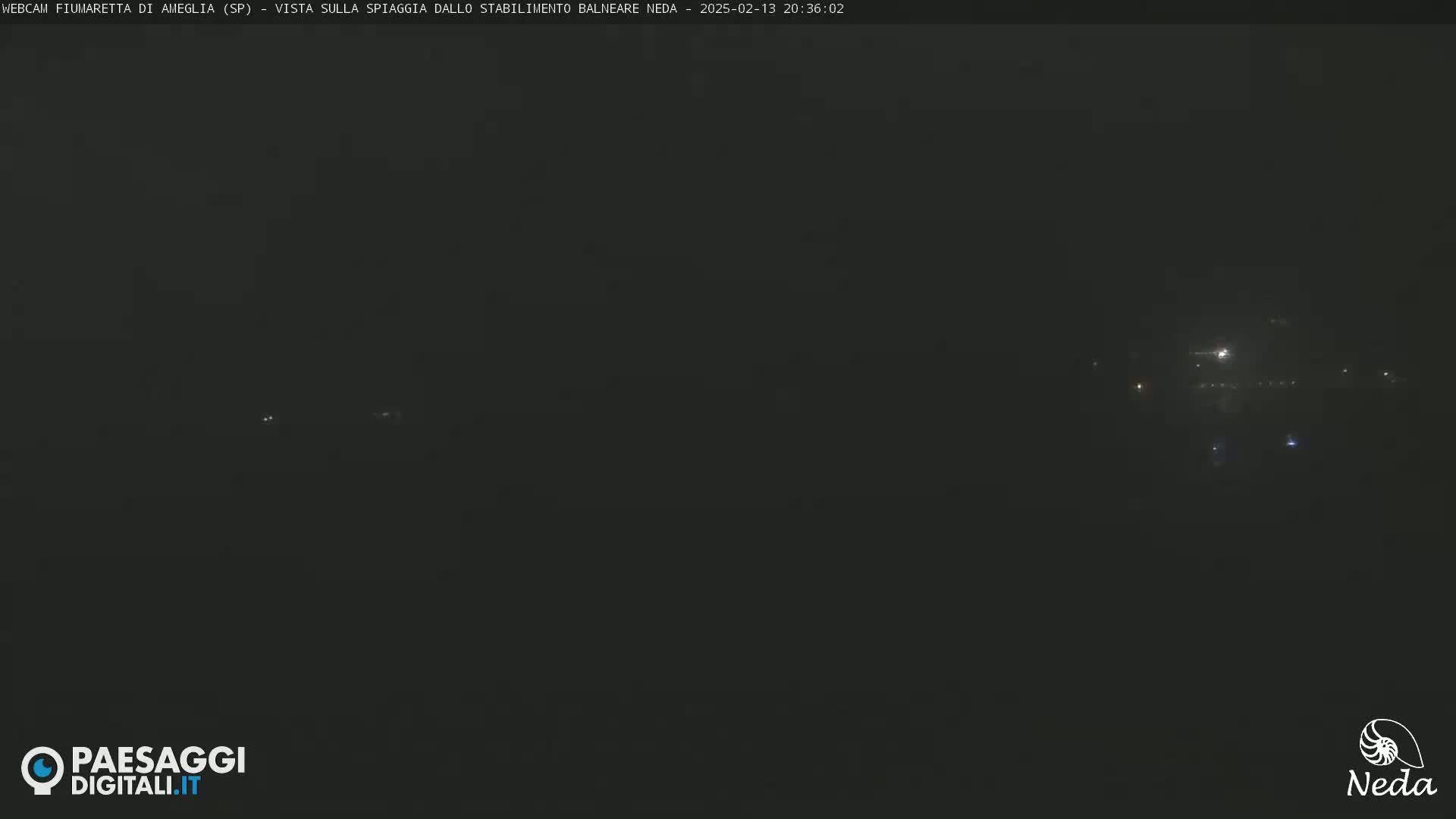 A dark, nighttime view of faintly lit buildings or structures in the distance.