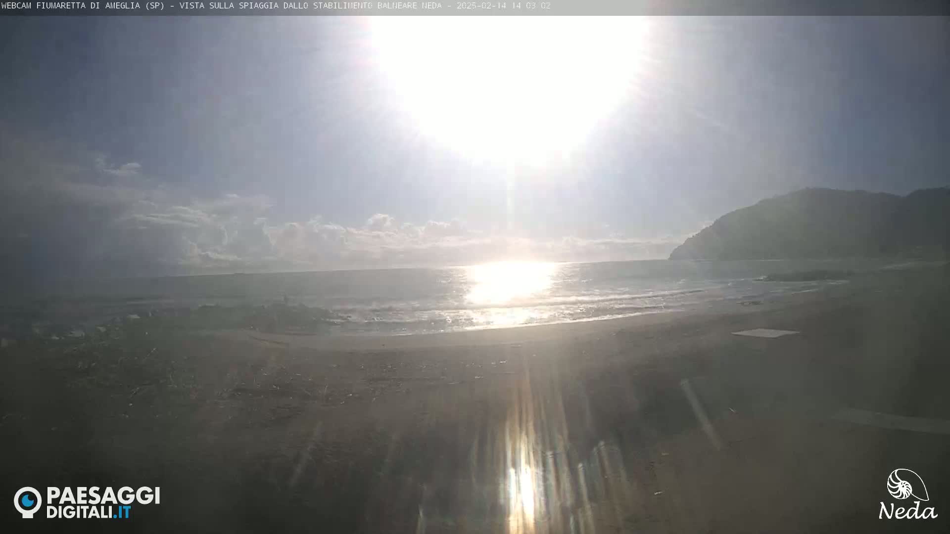 A sunny day at a beach with a calm sea and a hill in the background.