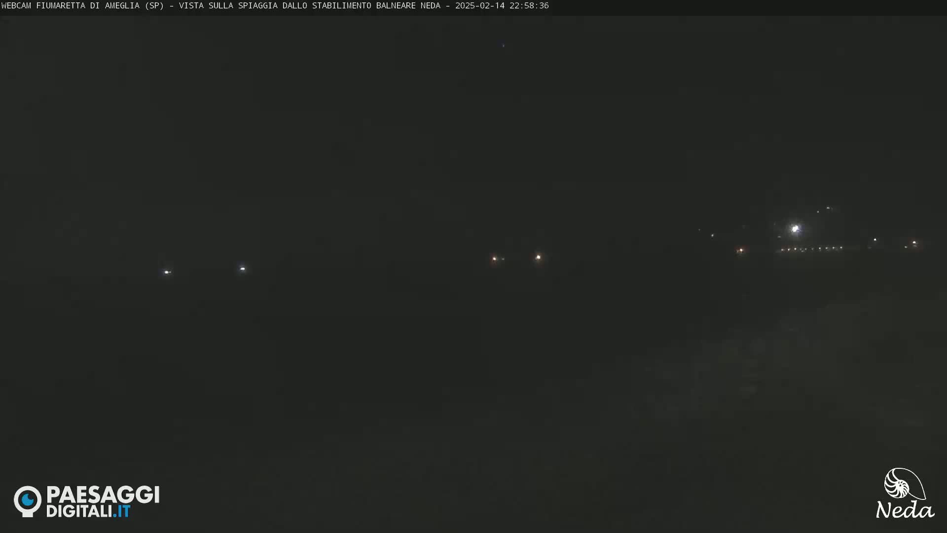 A nighttime view of a dark beach with a few faint lights visible in the distance.