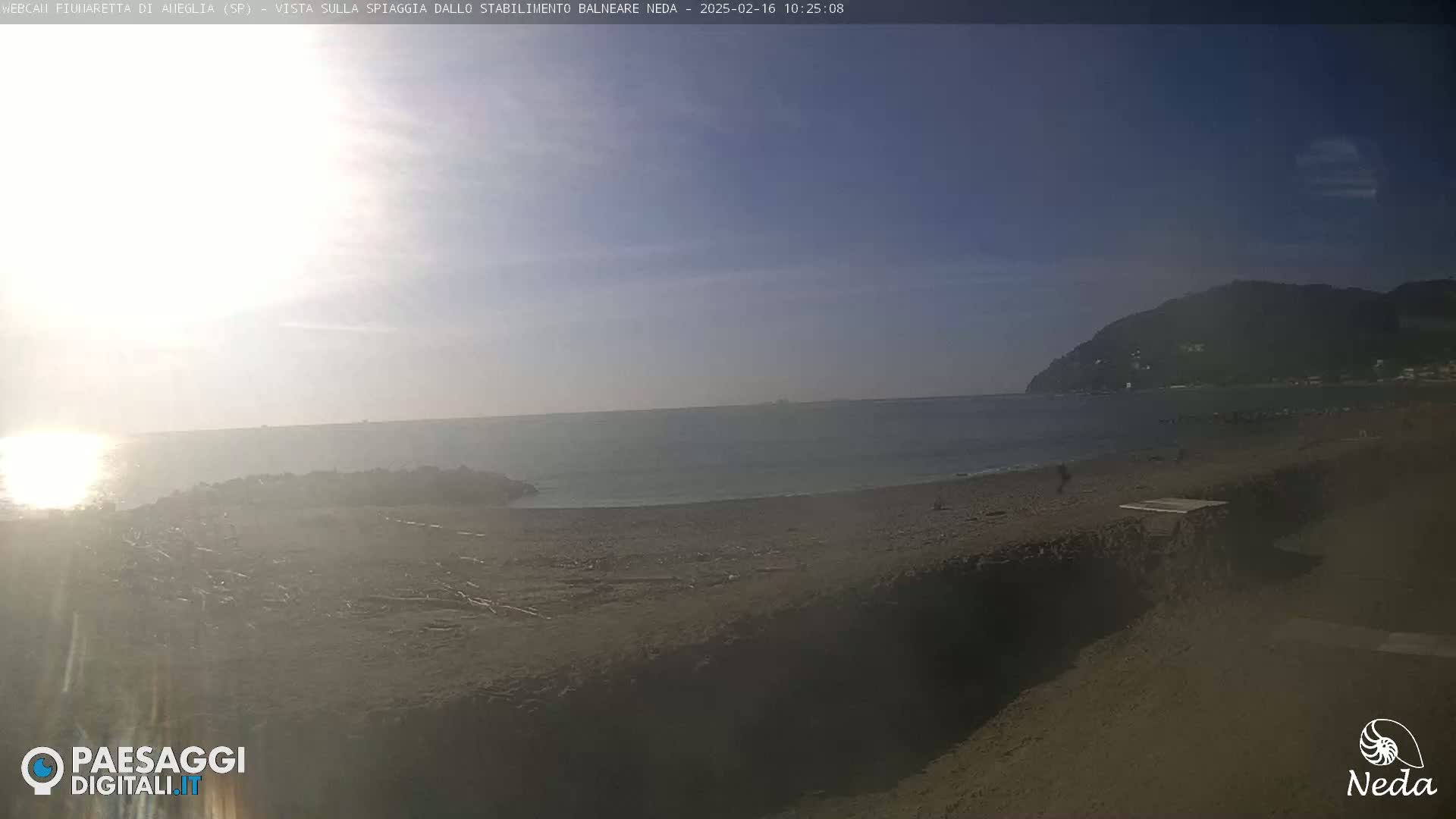 A sunny, mostly clear day at a beach with calm ocean water and a distant mountain in the background.