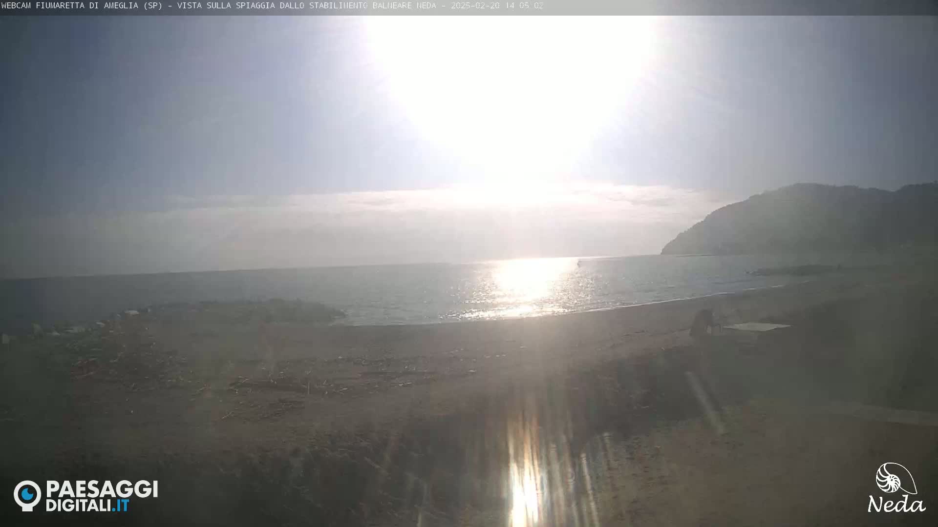 A sunny day at a beach, showing a calm sea with a distant mountain in the background.