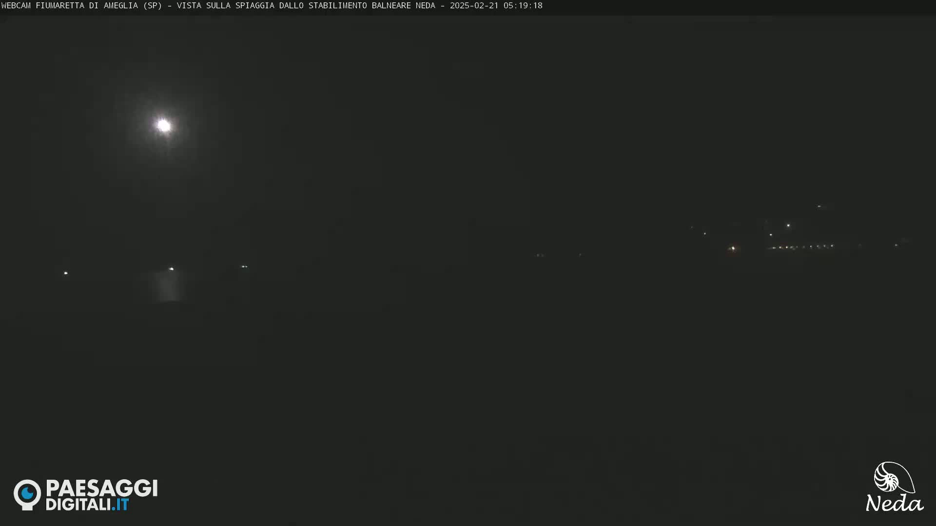 A bright moon illuminates a dark, nighttime scene of a beach viewed from a distance.
