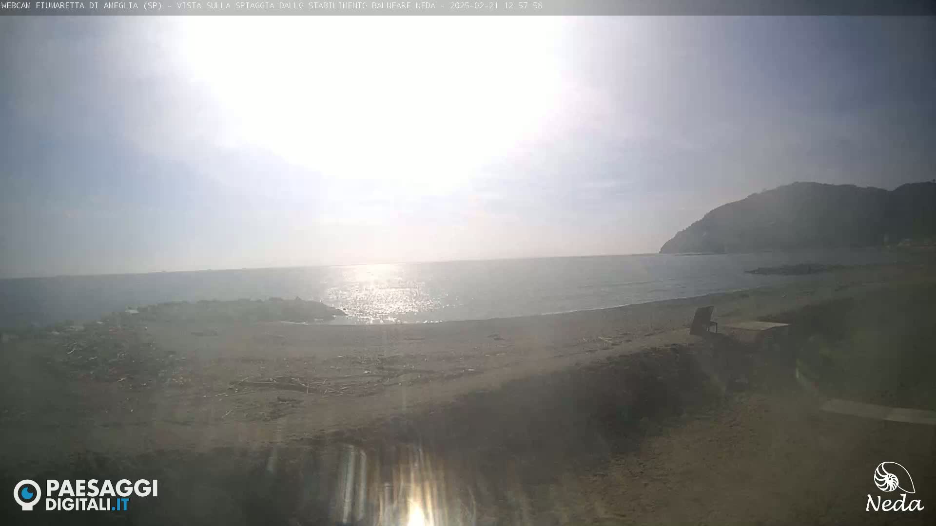 A hazy, sunny day at a beach with calm water, a sandy shore, and a distant hill.