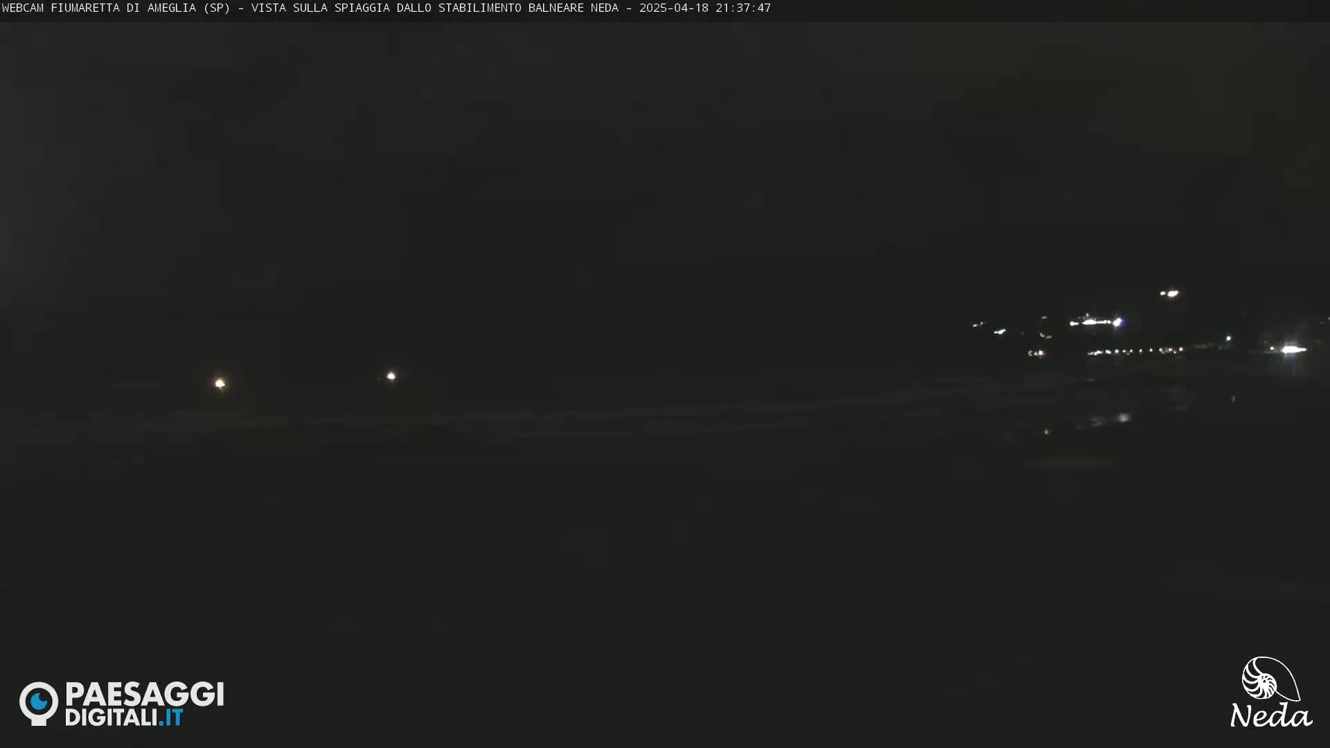 A dark, nighttime view of a beach with distant lights.