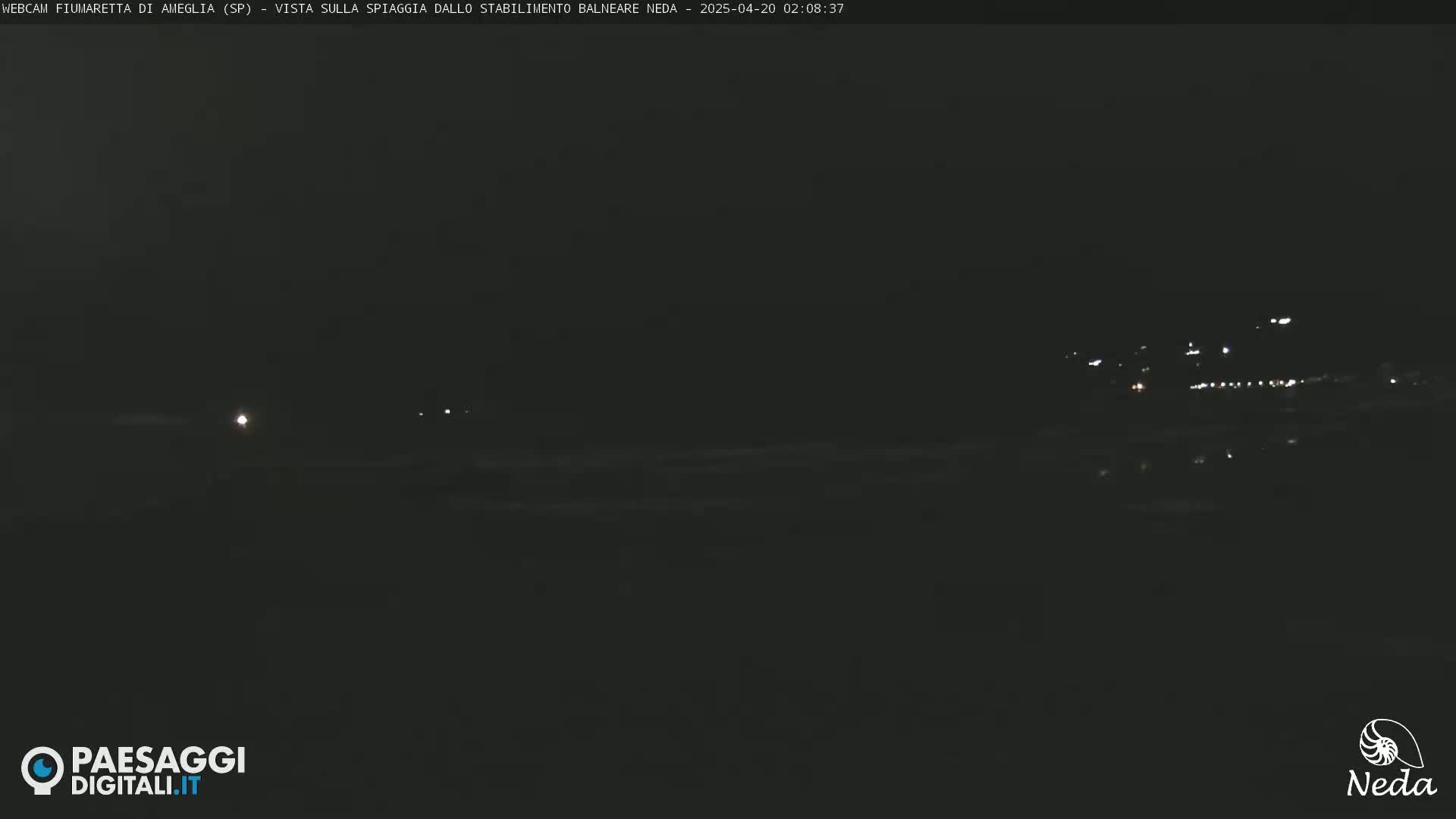 A dark nighttime view of a beach with faint lights visible in the distance.