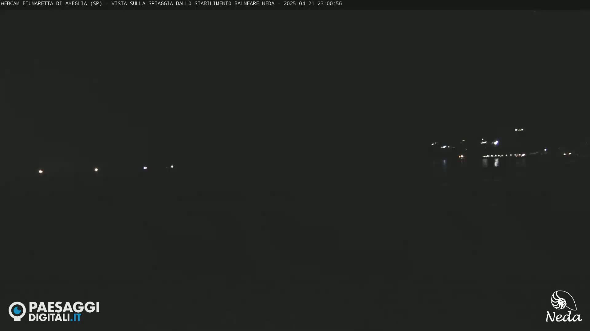A dark, nighttime scene shows a body of water reflecting faint lights from a distant shoreline.