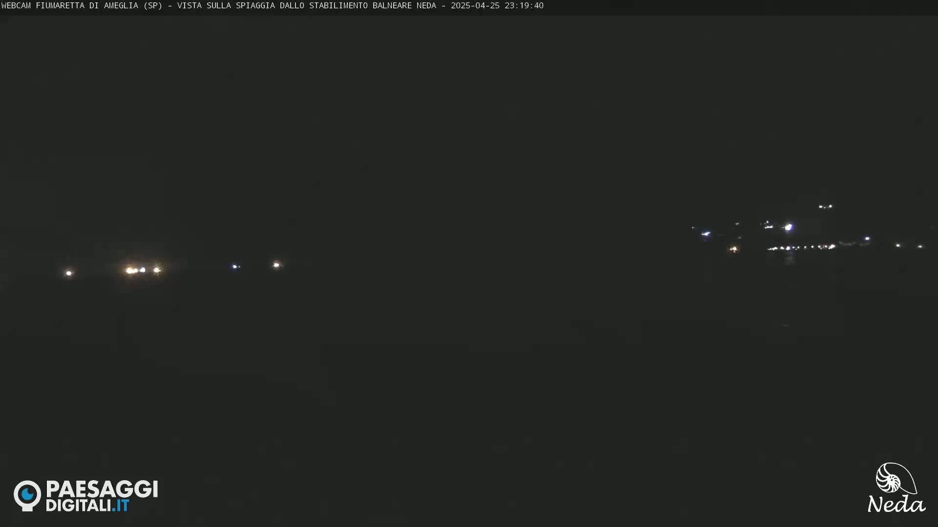 A nighttime long shot of a dark beach with a few distant lights visible.