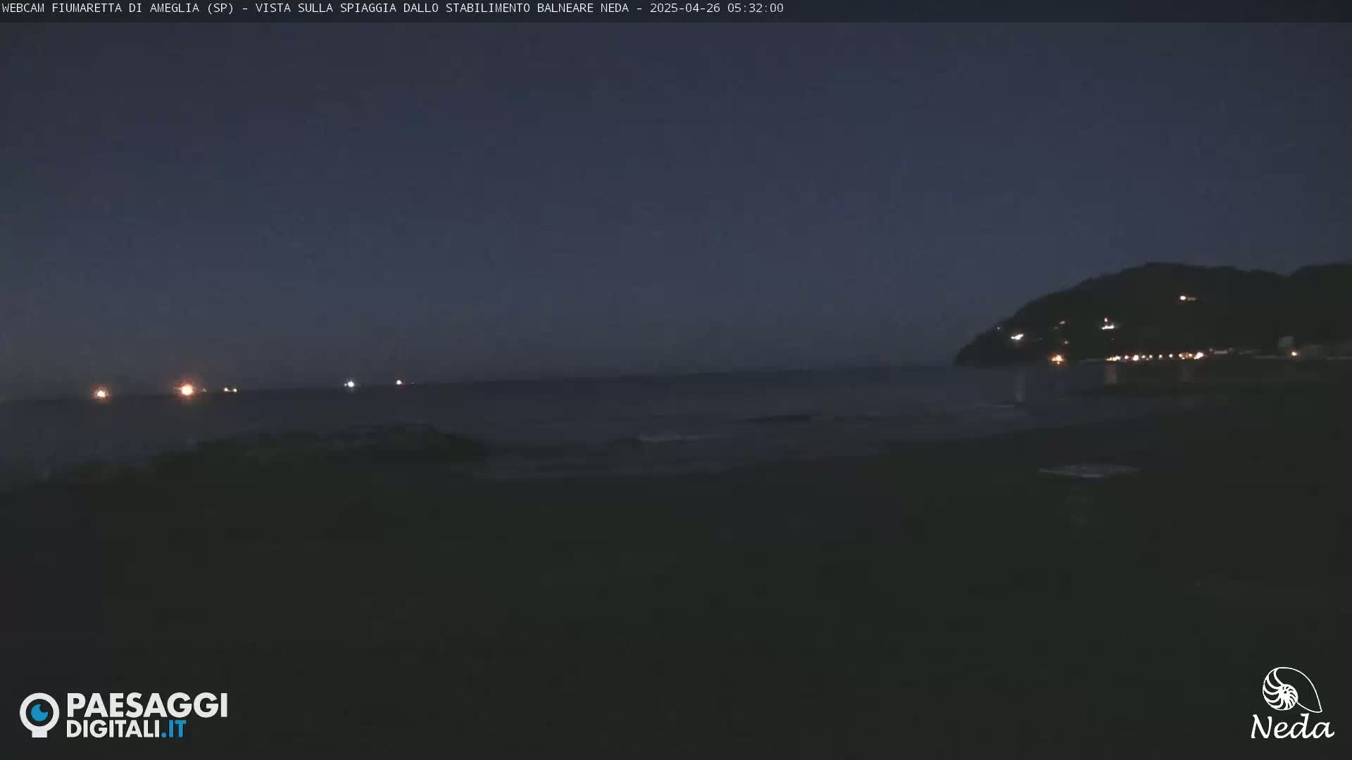 A dark, nighttime coastal scene shows a calm sea with distant lights on the water and a hill with scattered lights in the background.