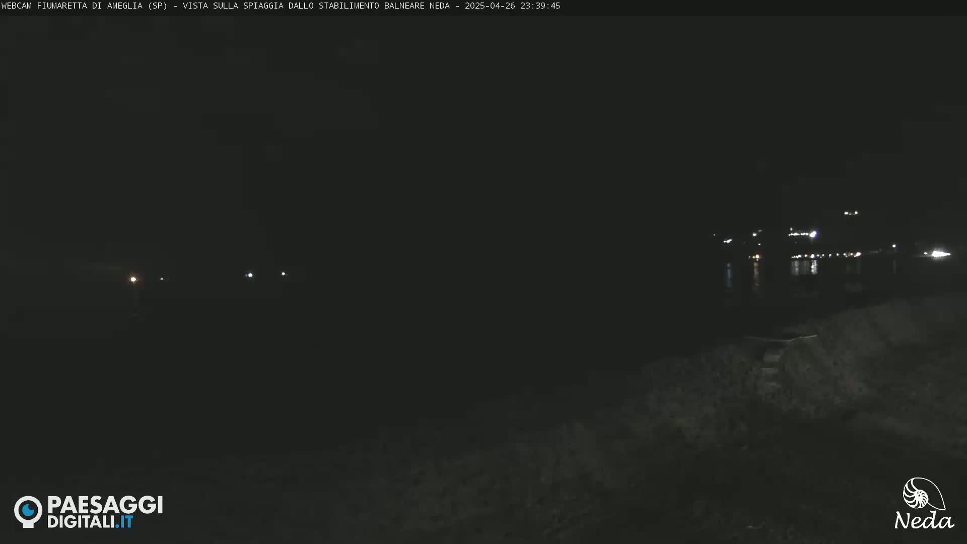 A dark nighttime beach scene shows distant lights across a body of water.