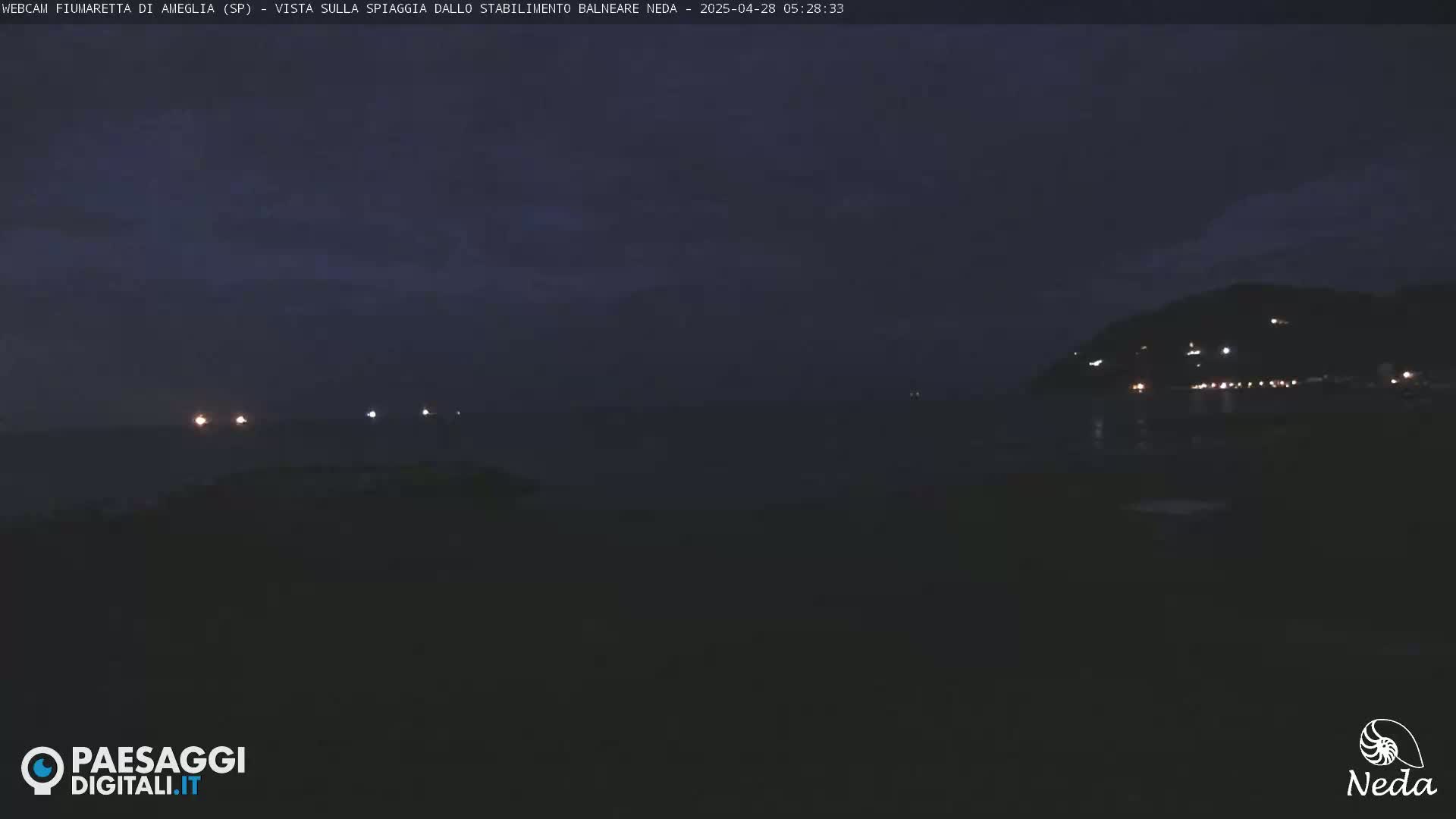 A dark, nighttime coastal scene shows a few faint lights on the water and a hillside with scattered lights in the distance under a mostly clear, dark sky.