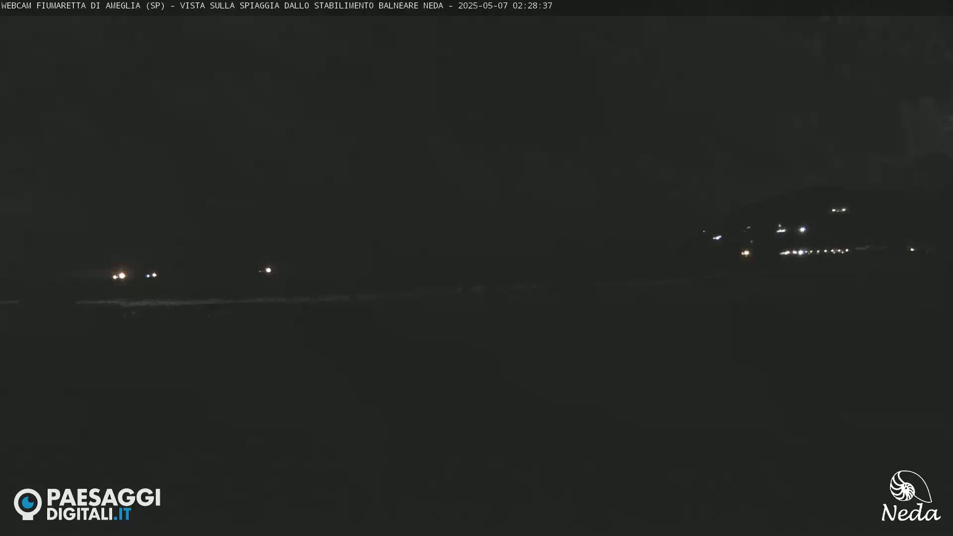 A dark, nighttime beach scene shows a few distant lights on the horizon.