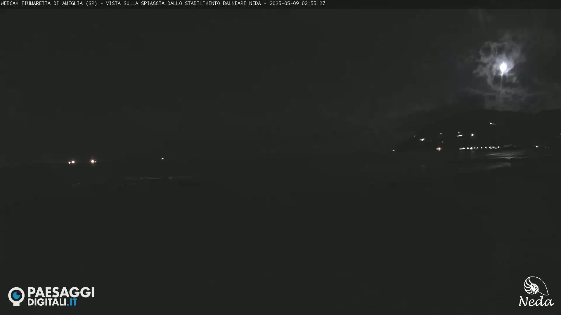A nighttime beach scene under a partly cloudy moonlit sky shows faint lights in the distance.