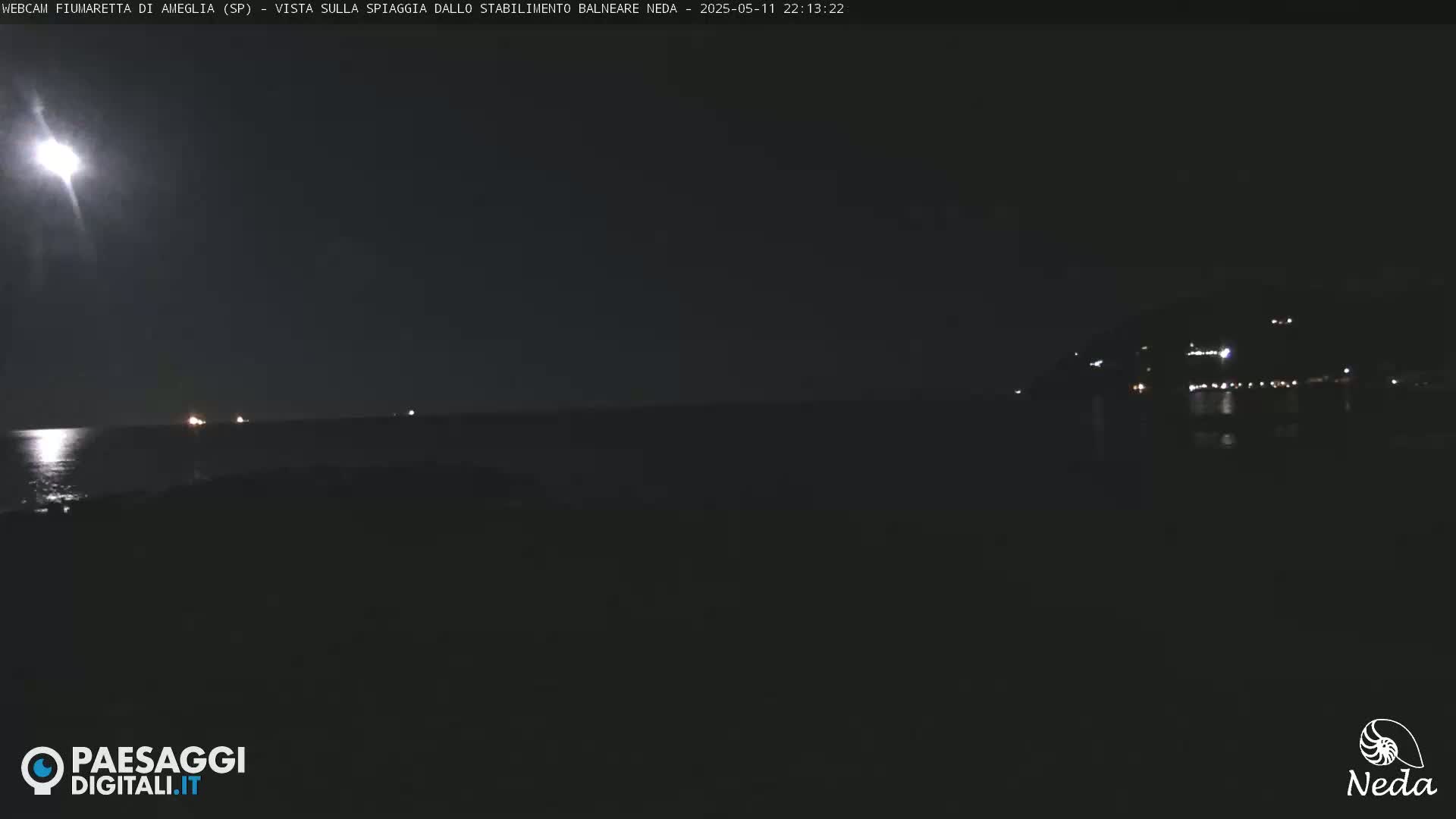 A nighttime coastal scene shows a bright moon reflecting on a dark sea, with faint lights visible on the horizon.