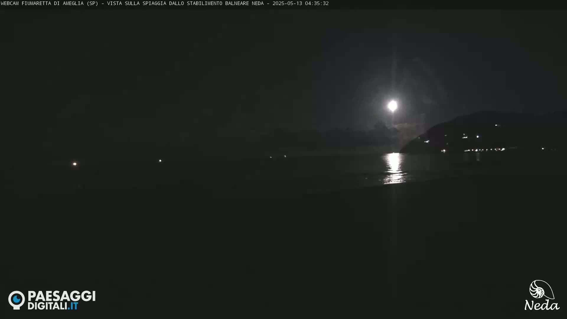 A bright moon illuminates a dark beach and distant hill at night.