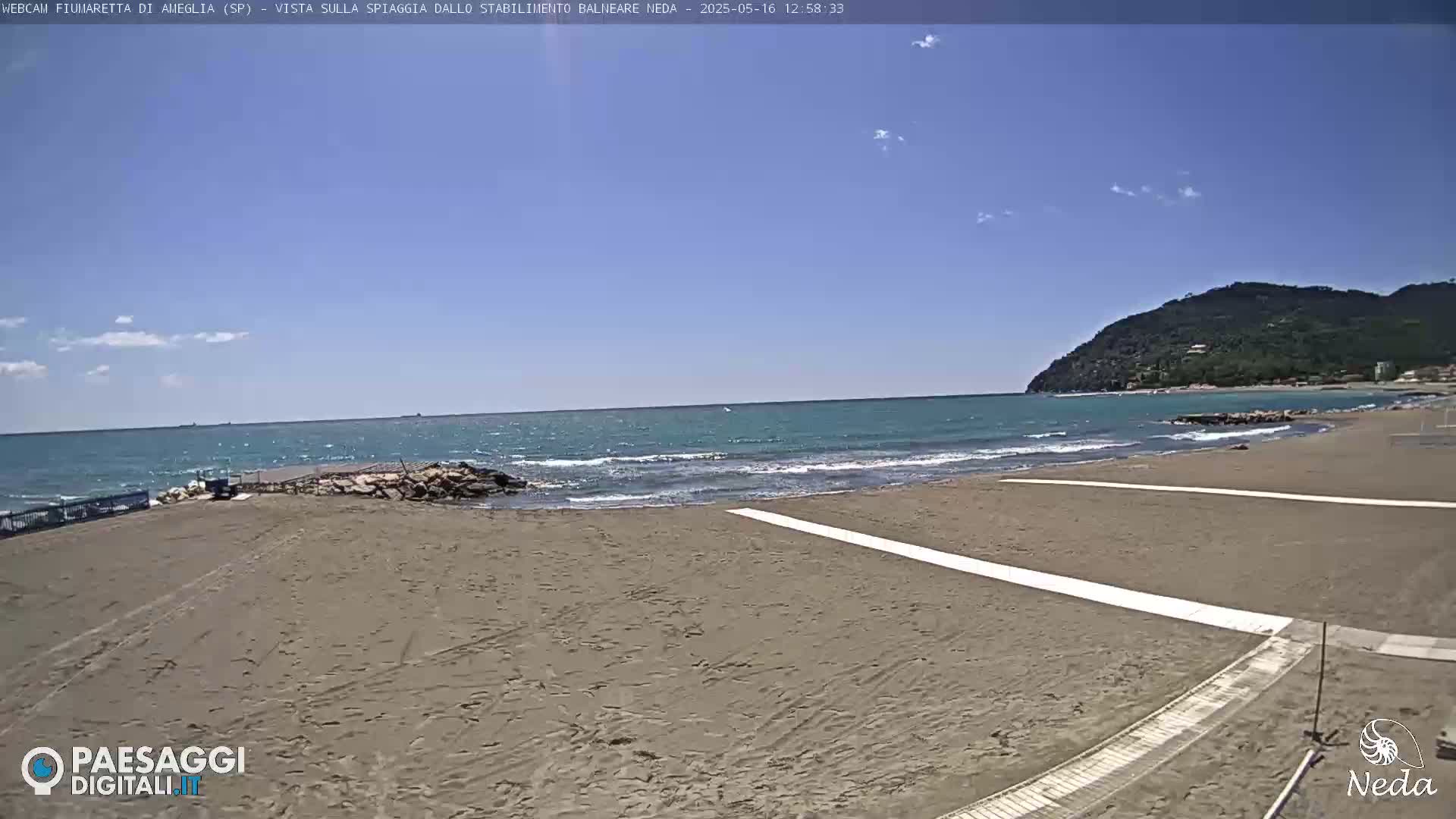 A sandy beach with a calm sea and a distant hill under a mostly clear sky.