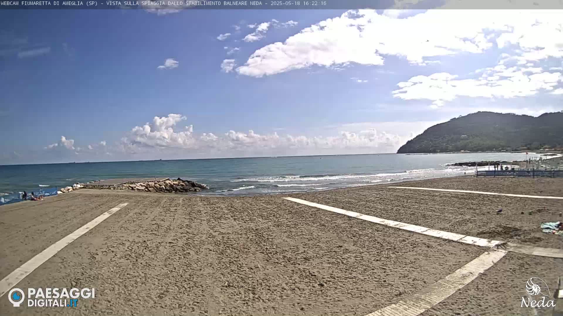 A sandy beach with a calm ocean under a partly cloudy sky stretches toward a distant hill.