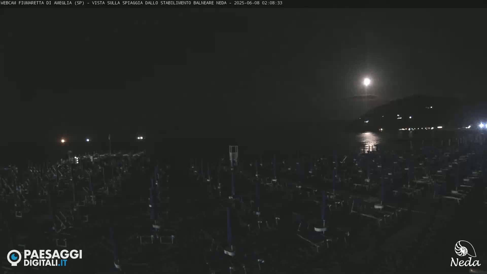 A nighttime beach scene shows a large number of closed beach umbrellas under a bright moon.