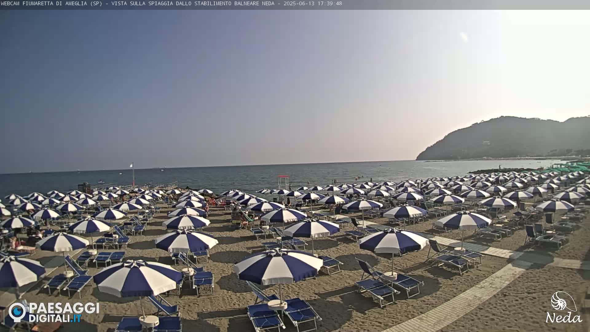 A sandy beach with numerous blue and white striped umbrellas under a clear sky and calm ocean.