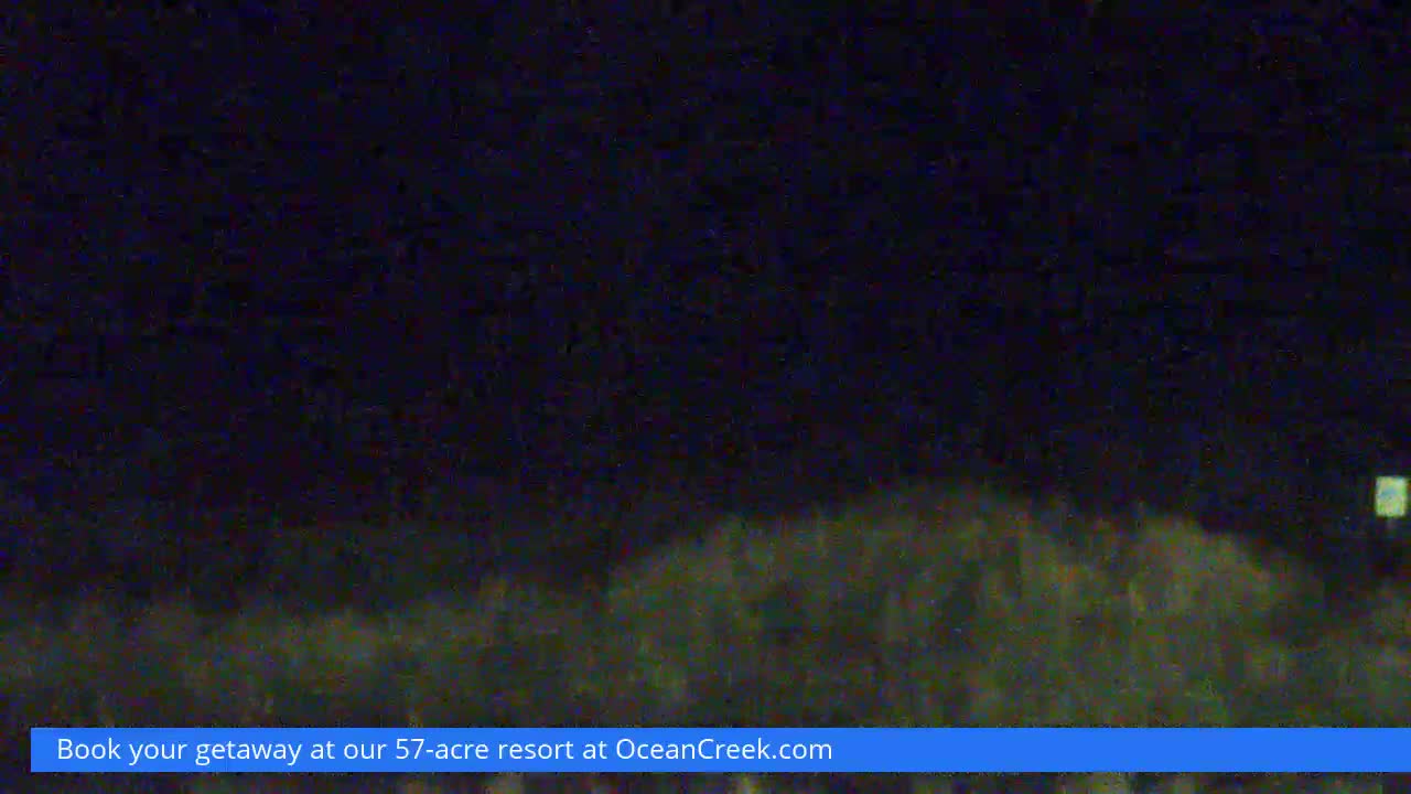 The image displays a very dark and grainy outdoor scene at night, with a vague horizon line separating a dark, indistinct foreground from an equally dark sky, and a faint rectangular light visible on the far right.