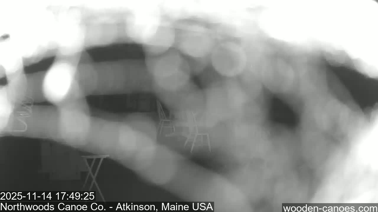 A highly blurred and grayscale outdoor patio scene, featuring faint outlines of chairs and a table, is largely obscured by extreme lens bokeh and haziness, likely indicating rainy or very misty weather conditions.