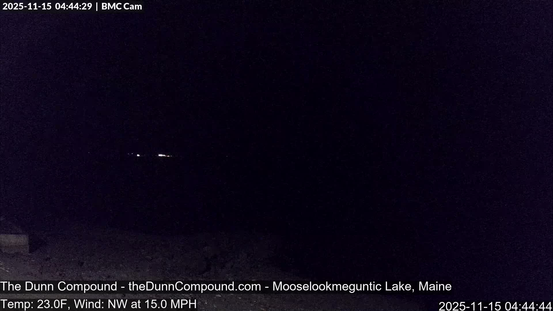 A very dark, clear night scene shows a few distant white lights glowing faintly in the distance above a shadowy, indistinct foreground.