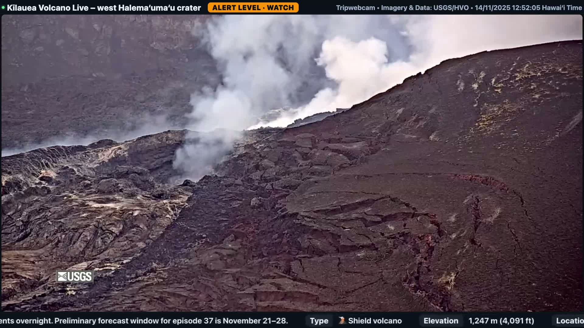 A vast, dark, rugged volcanic crater shows white steam rising from various fissures across its rocky, fractured terrain under a partly cloudy sky.