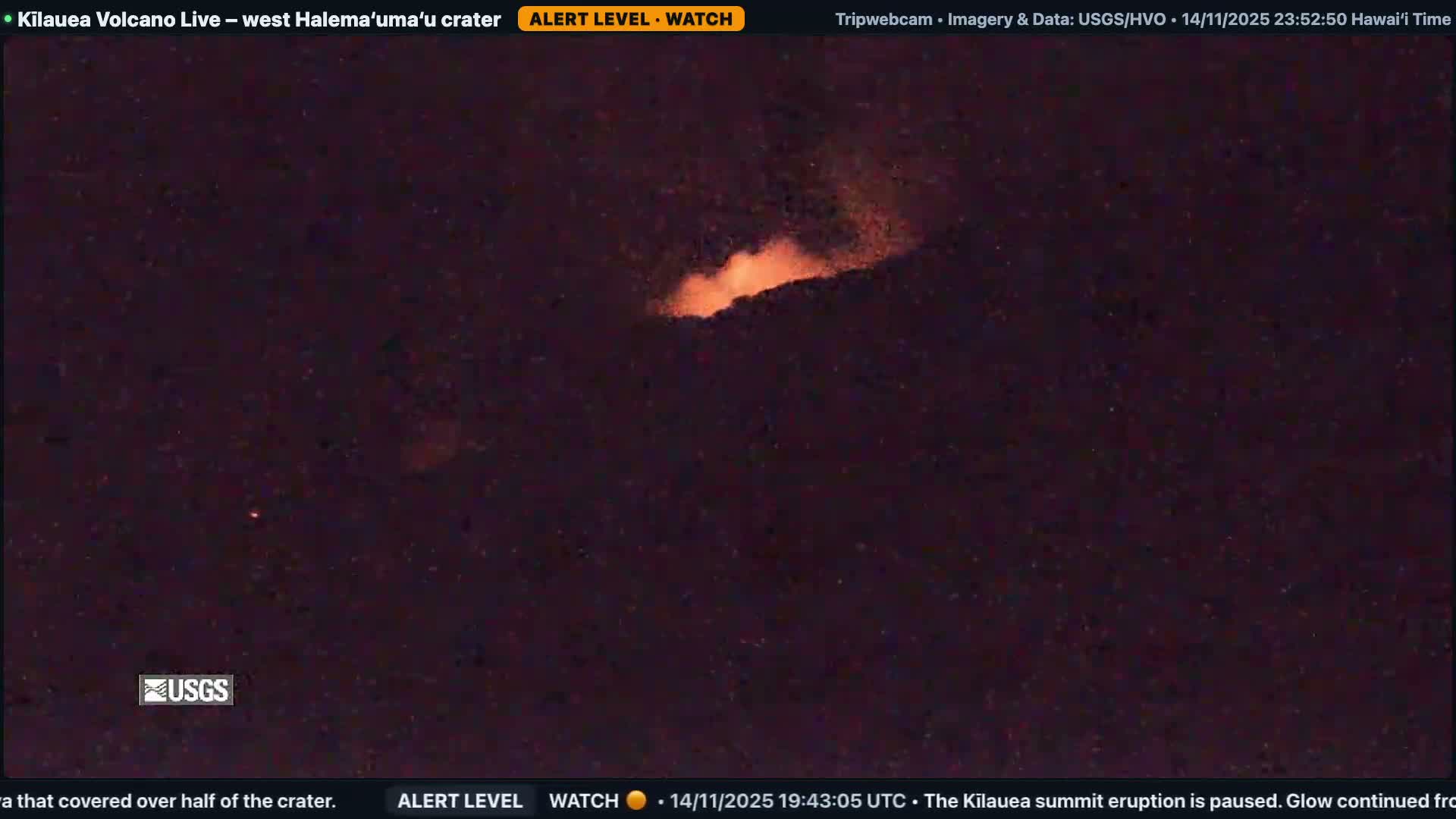 A dark, nighttime image captures a bright orange, fiery glow emanating from a rocky crevice or crater in an otherwise dark landscape, under clear skies.