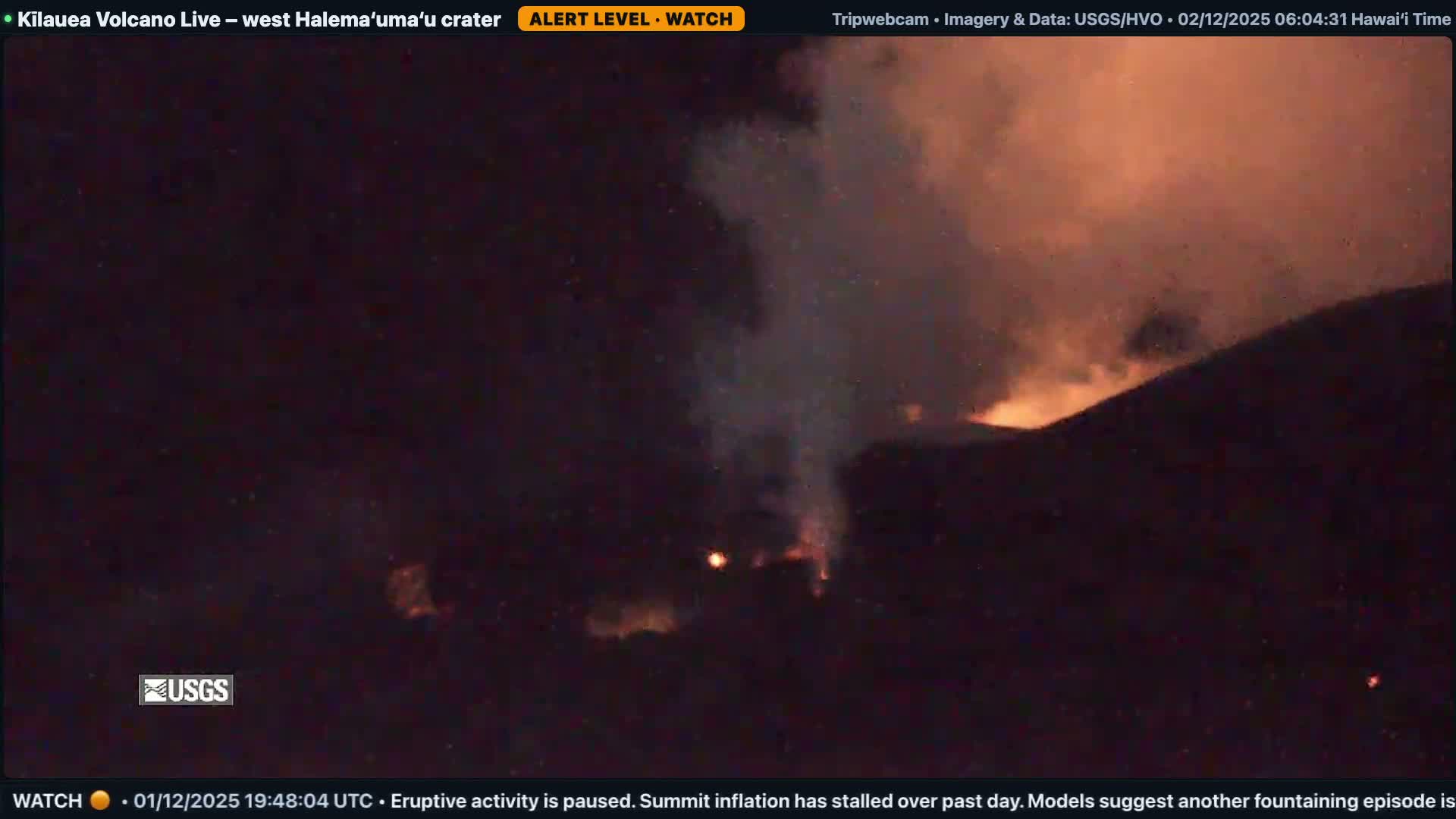 At night, a volcano erupts, illuminating the dark sky with an intense orange-red glow from flowing lava and a large plume of smoke and ash.